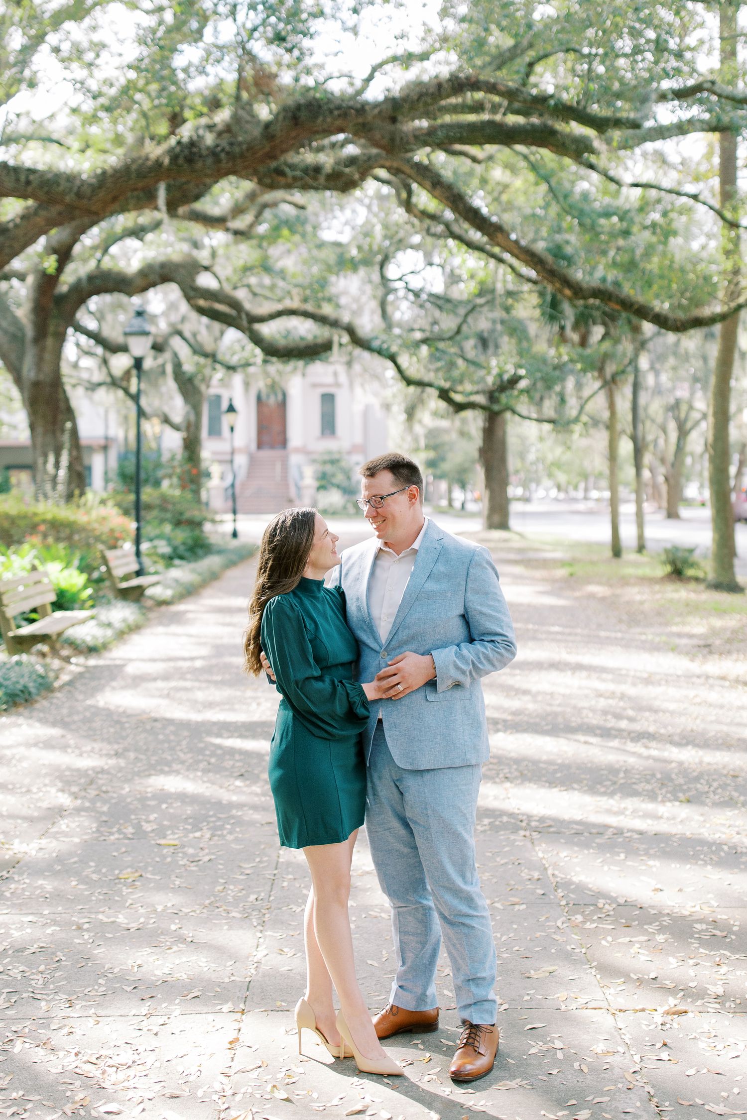 A couple shares a romantic moment under gorgeous moss-draped oak trees on a sunlit path.