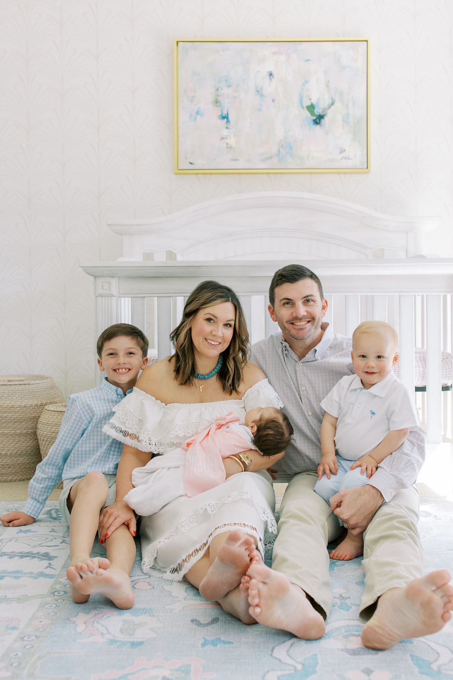 Family portrait in a bright nursery with pastel artwork and white furniture.