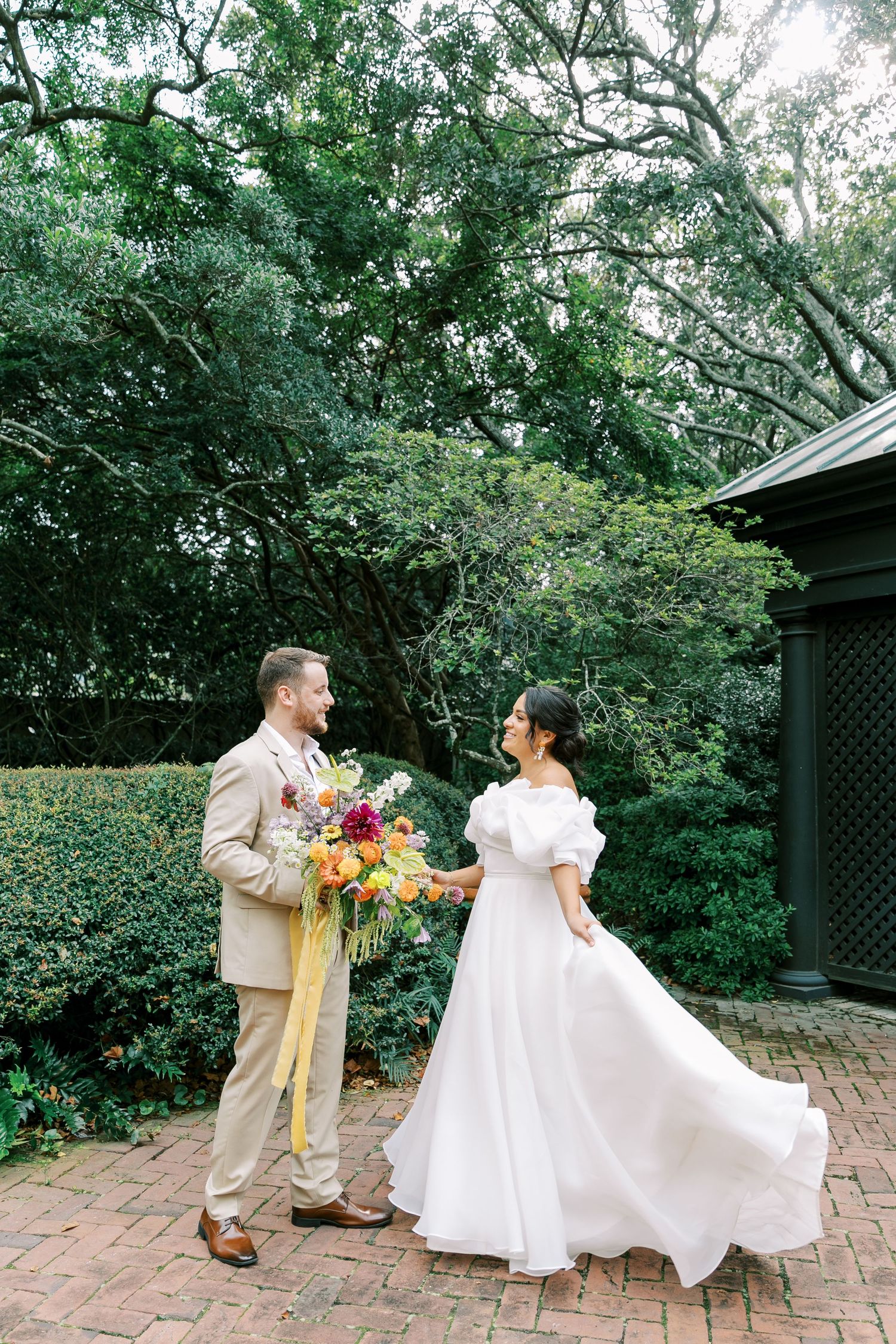 Newlyweds share a joyful moment in a lush garden setting with the bride wearing a flowing white dress.