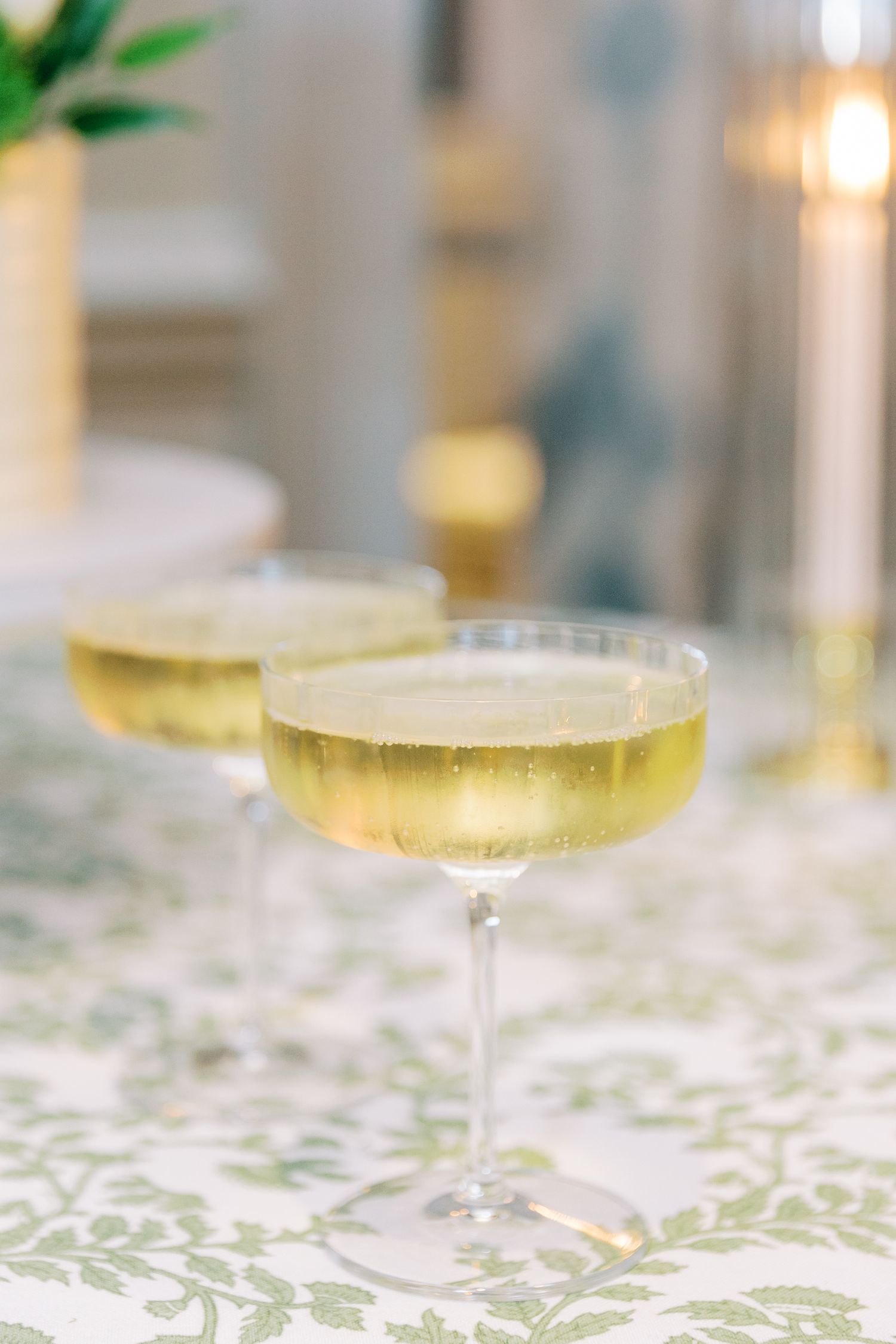 Two champagne coupe glasses filled with sparkling wine on a decorative tablecloth.