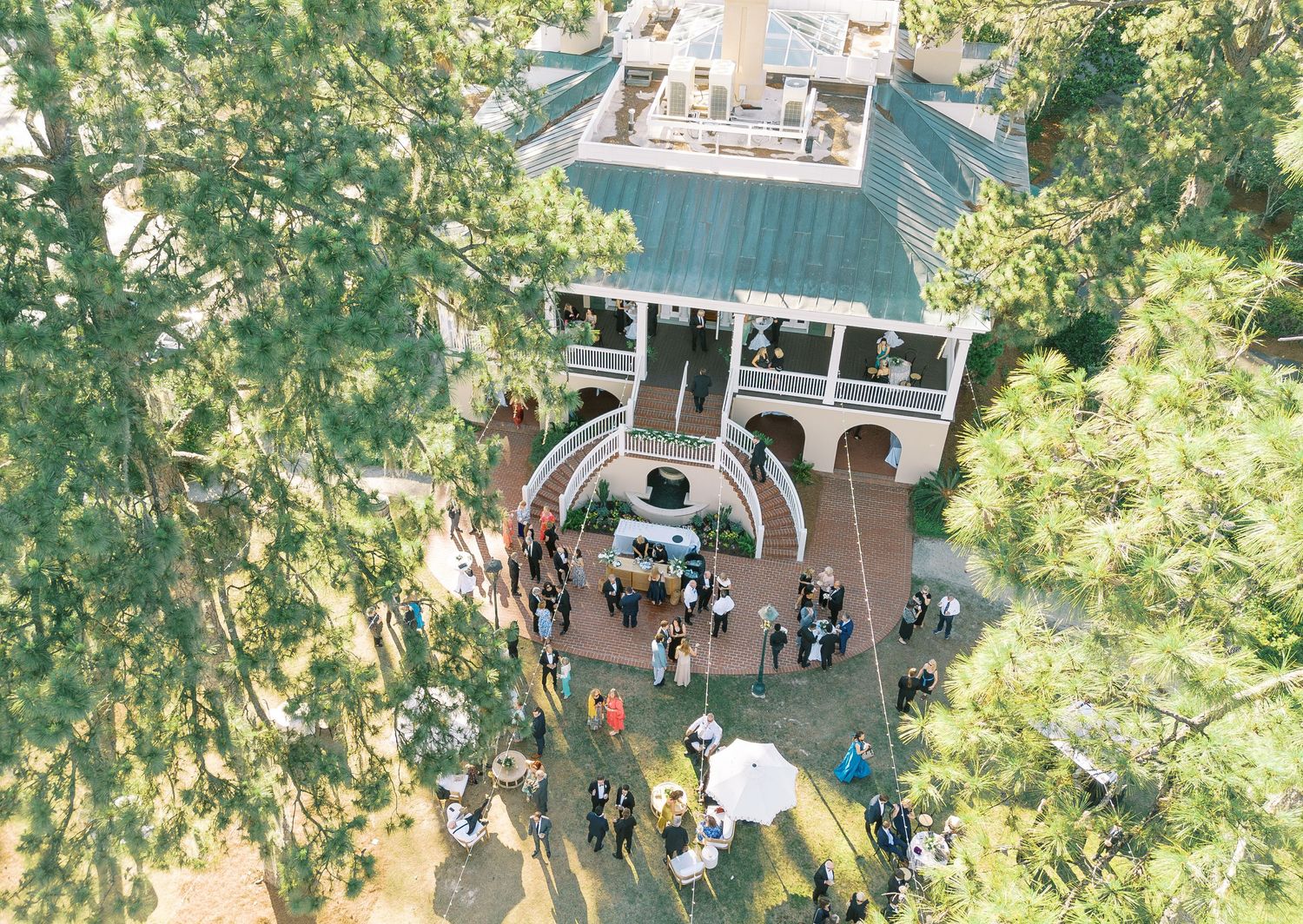 Aerial view of a gazebo-style structure with a turquoise roof surrounded by trees and people gathering below.