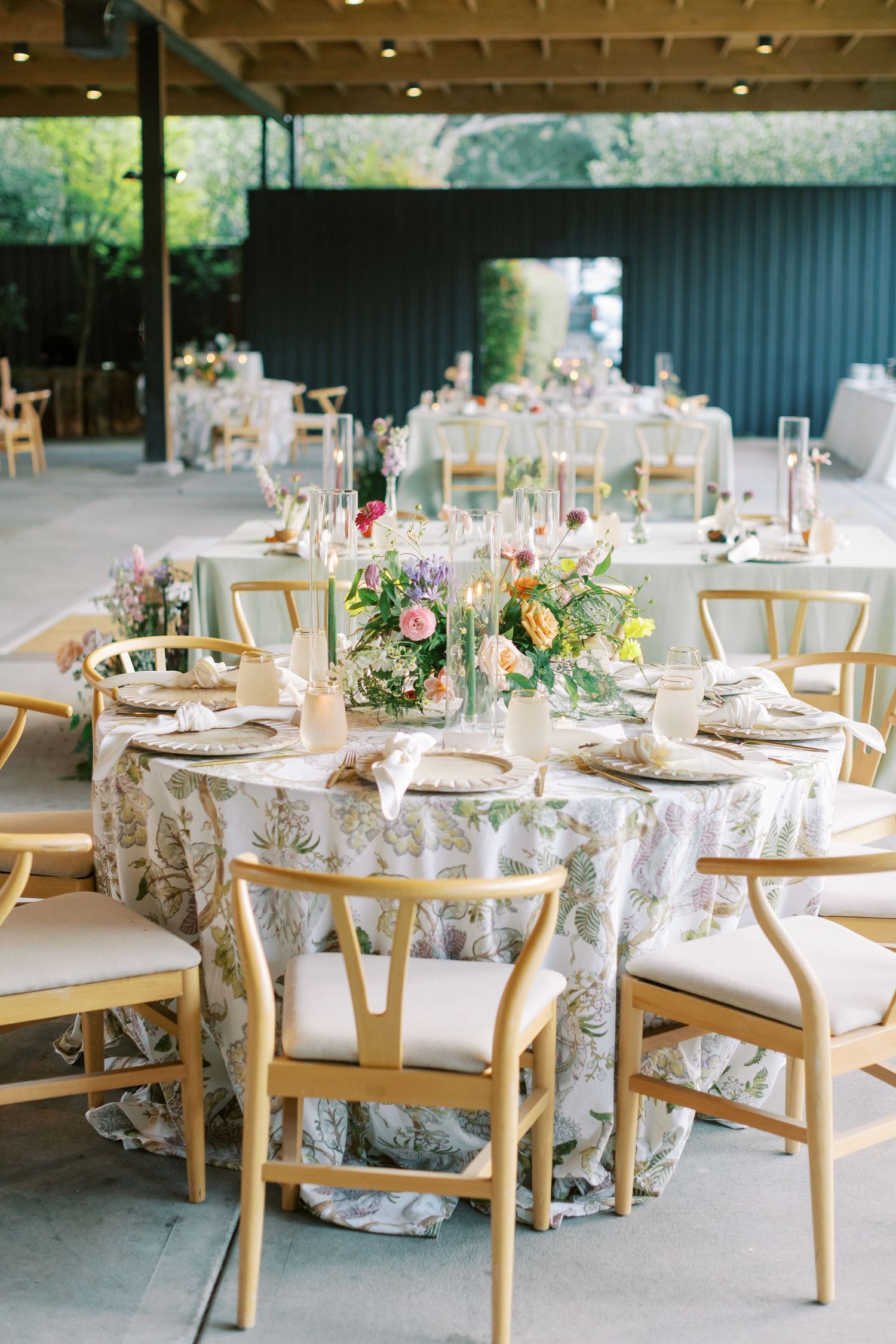 Wedding reception tables set with elegant place settings, floral arrangements, and wooden chairs.