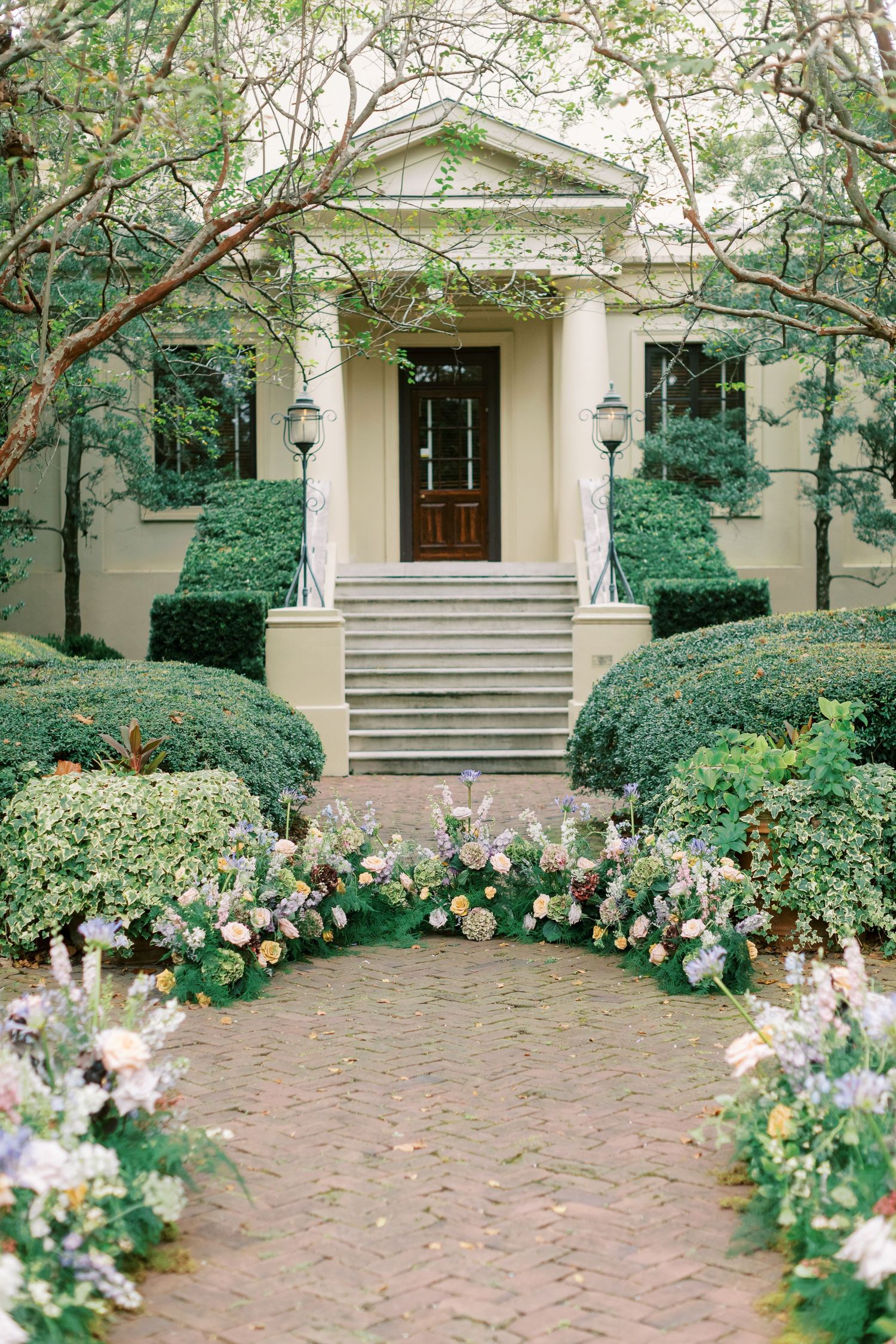 A stately colonial-style entrance with white columns and manicured bushes adorned with pink and white floral arrangements.