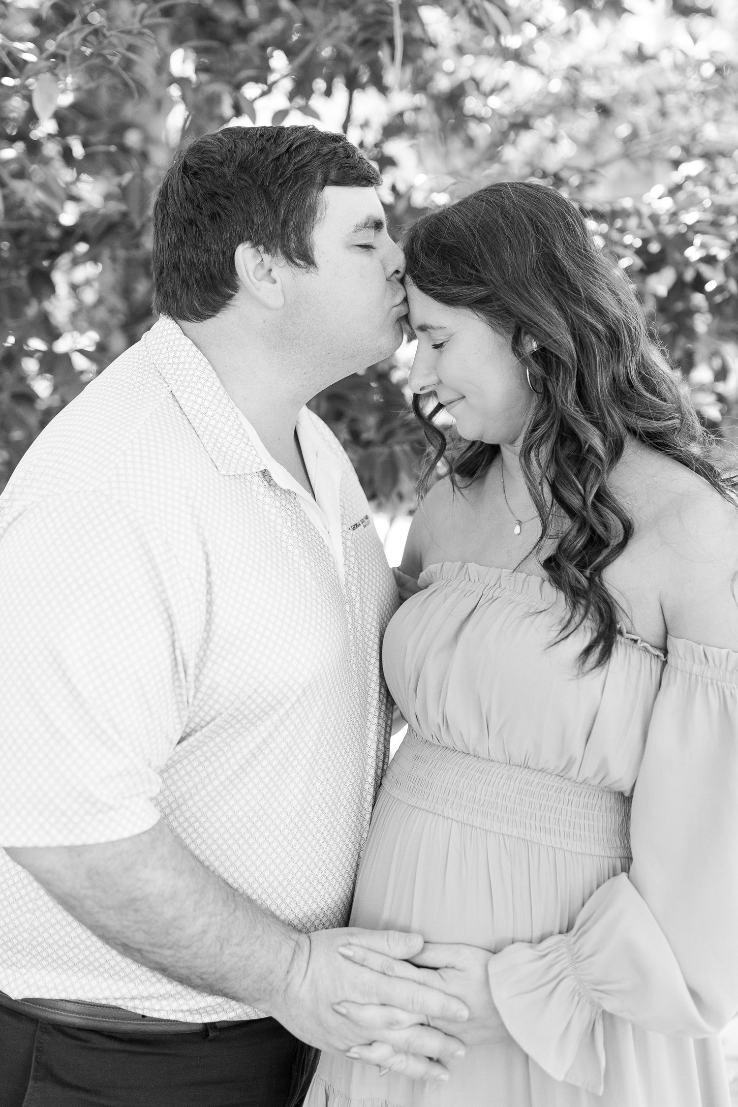 A romantic black and white maternity photo showing an intimate couple moment outdoors.