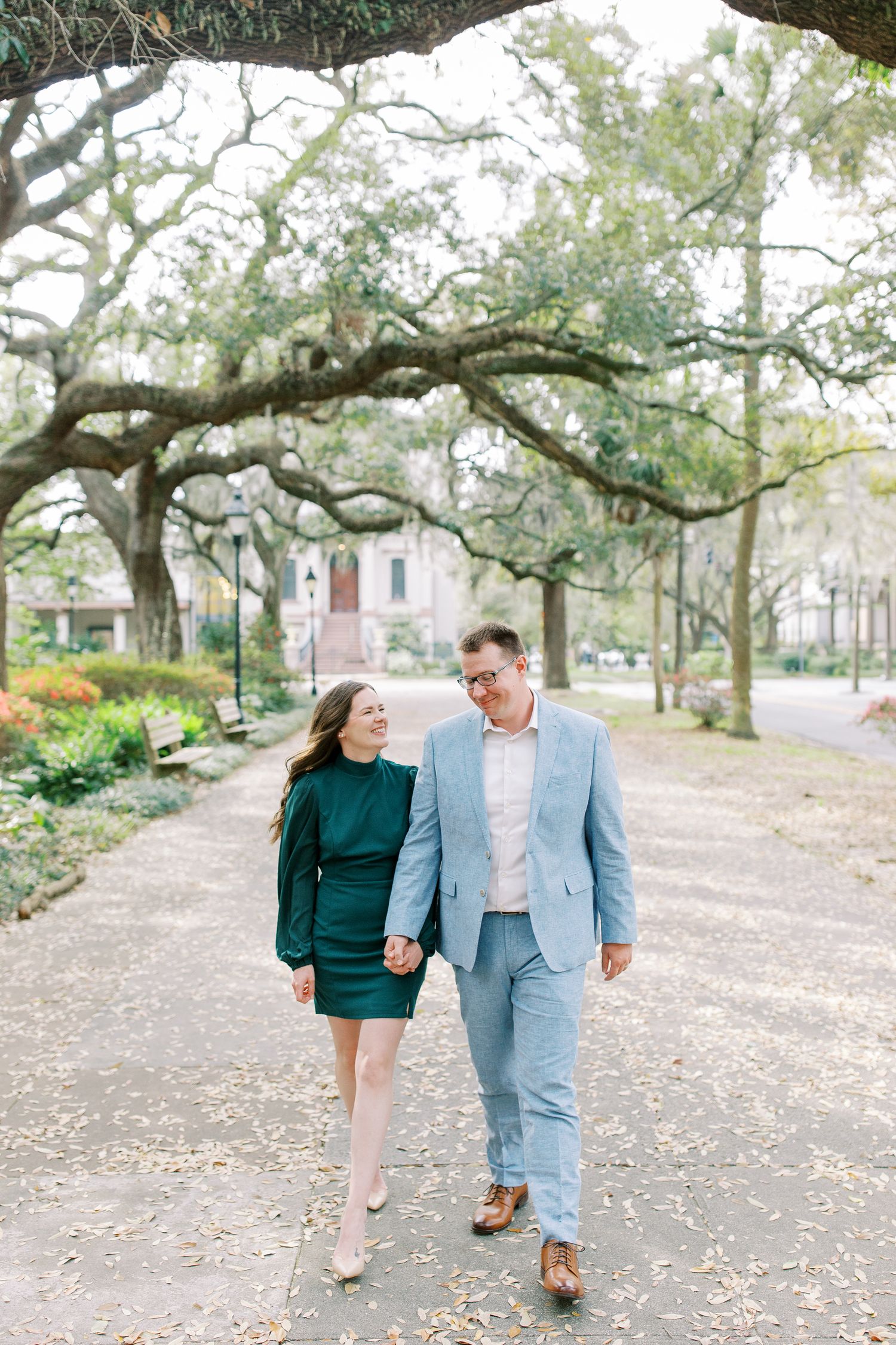 A couple walks hand in hand under Spanish moss-draped trees along a garden path.