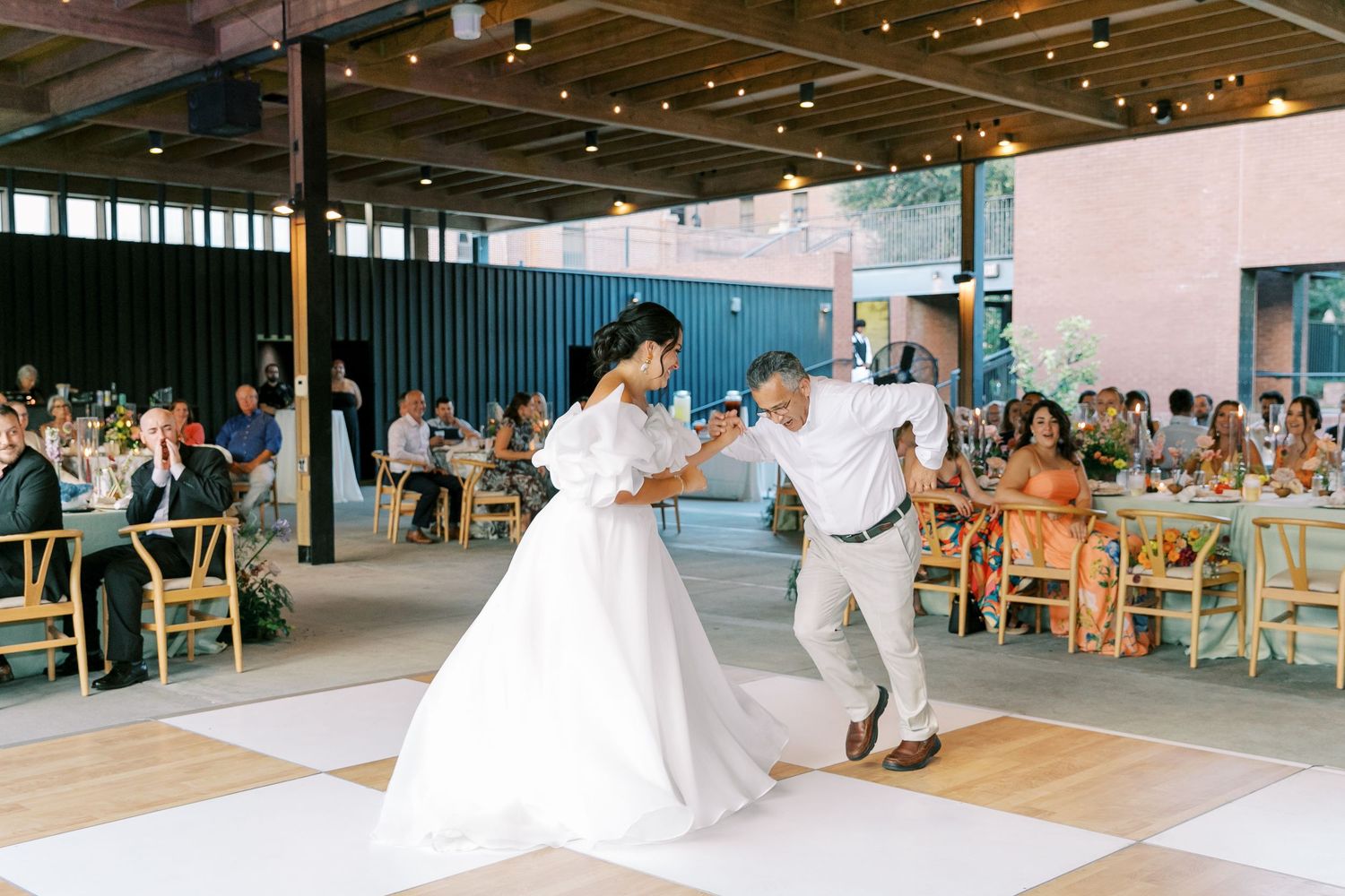 A couple shares their first dance at their wedding reception while guests watch from wooden chairs.