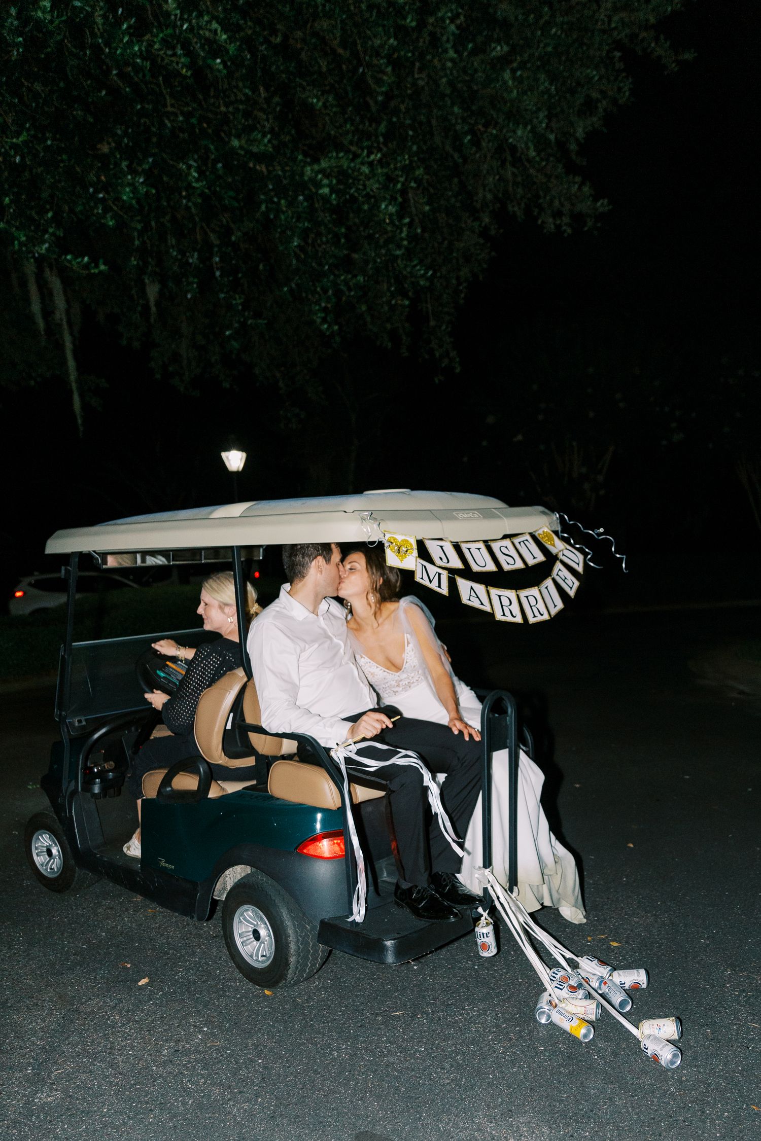 Newlyweds share a romantic moment in a decorated golf cart at night.