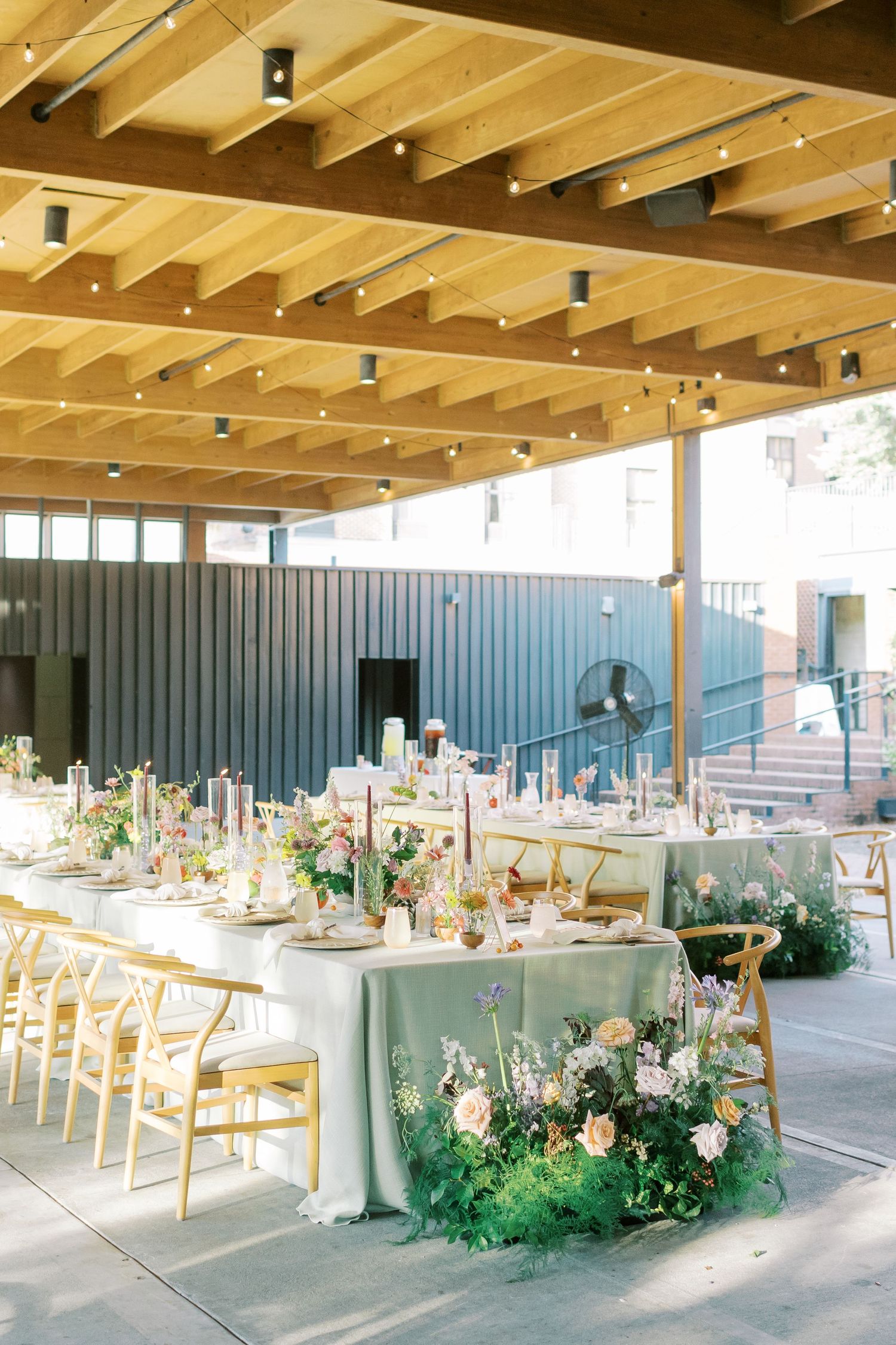 A modern wedding reception space decorated with floral centerpieces and wooden ceiling beams.