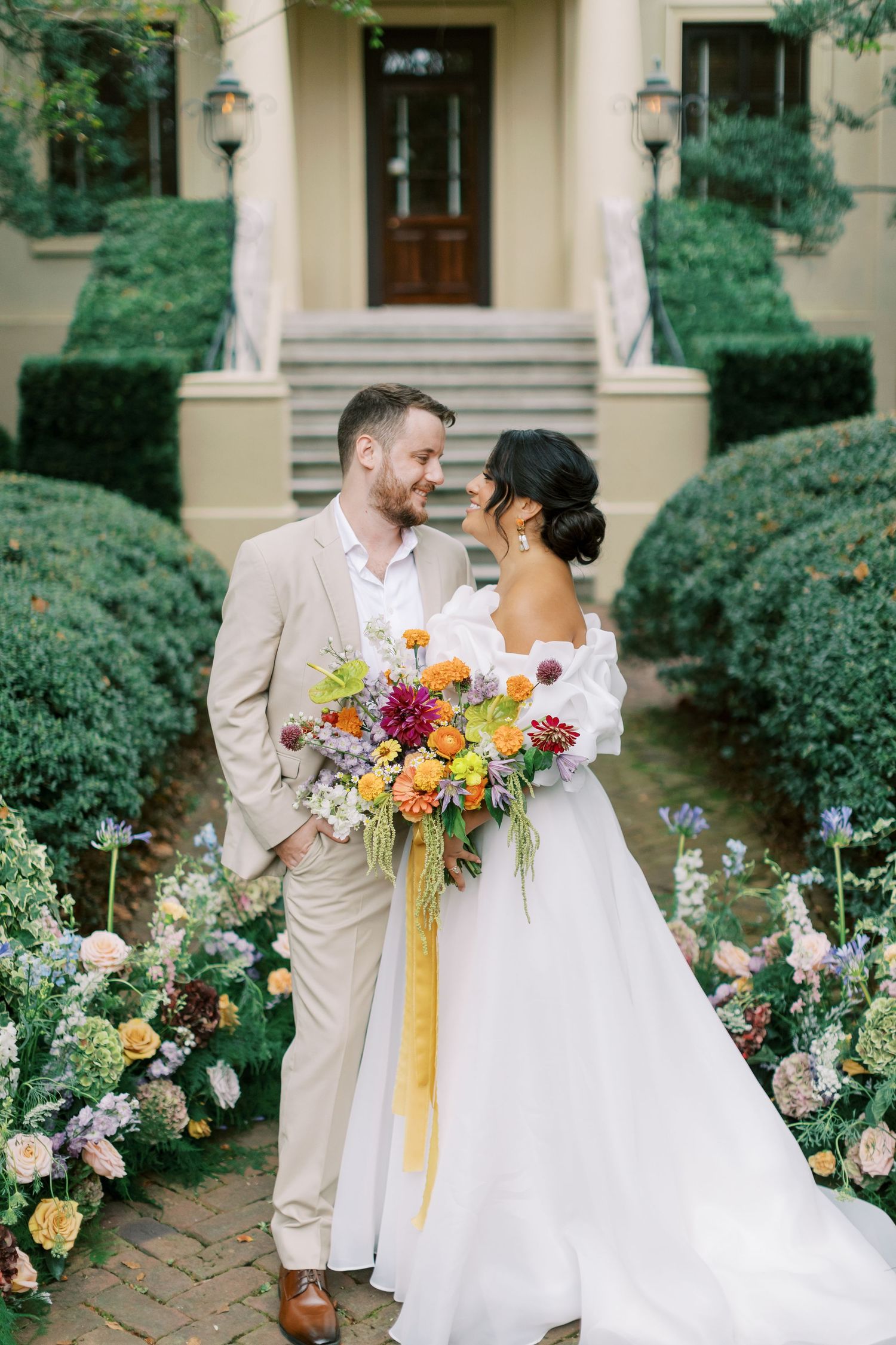 Elegant wedding couple posing by stone steps with beautiful landscaping and a colorful floral bouquet.