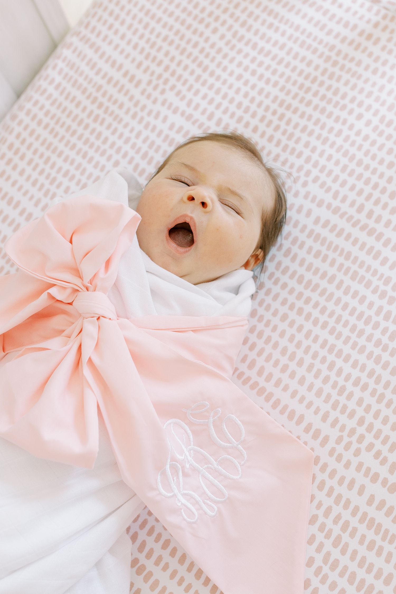 Sleeping baby wearing white with large pink bow on textured bedding.