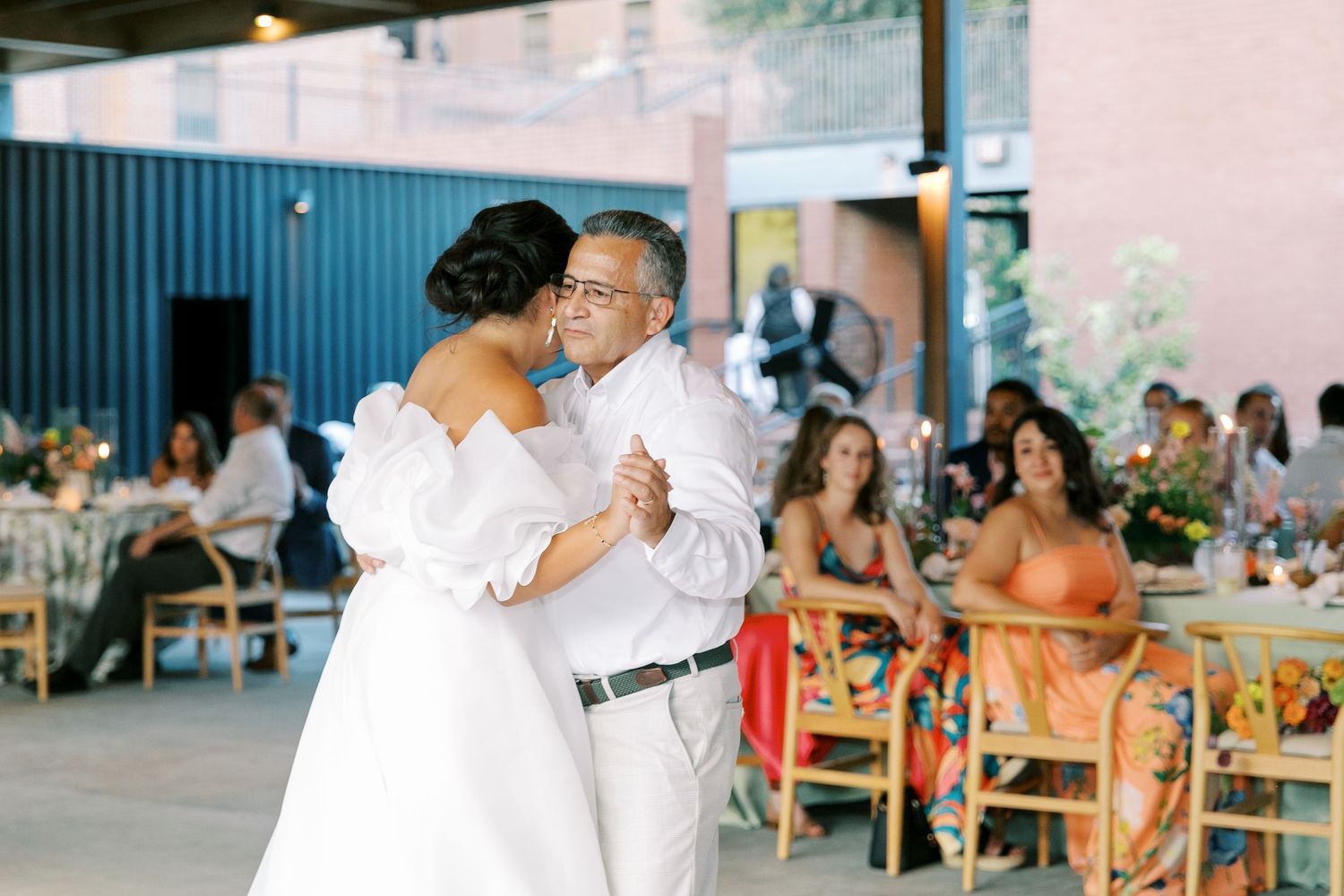 Wedding celebration dancing in a covered pavilion space with festive lighting.