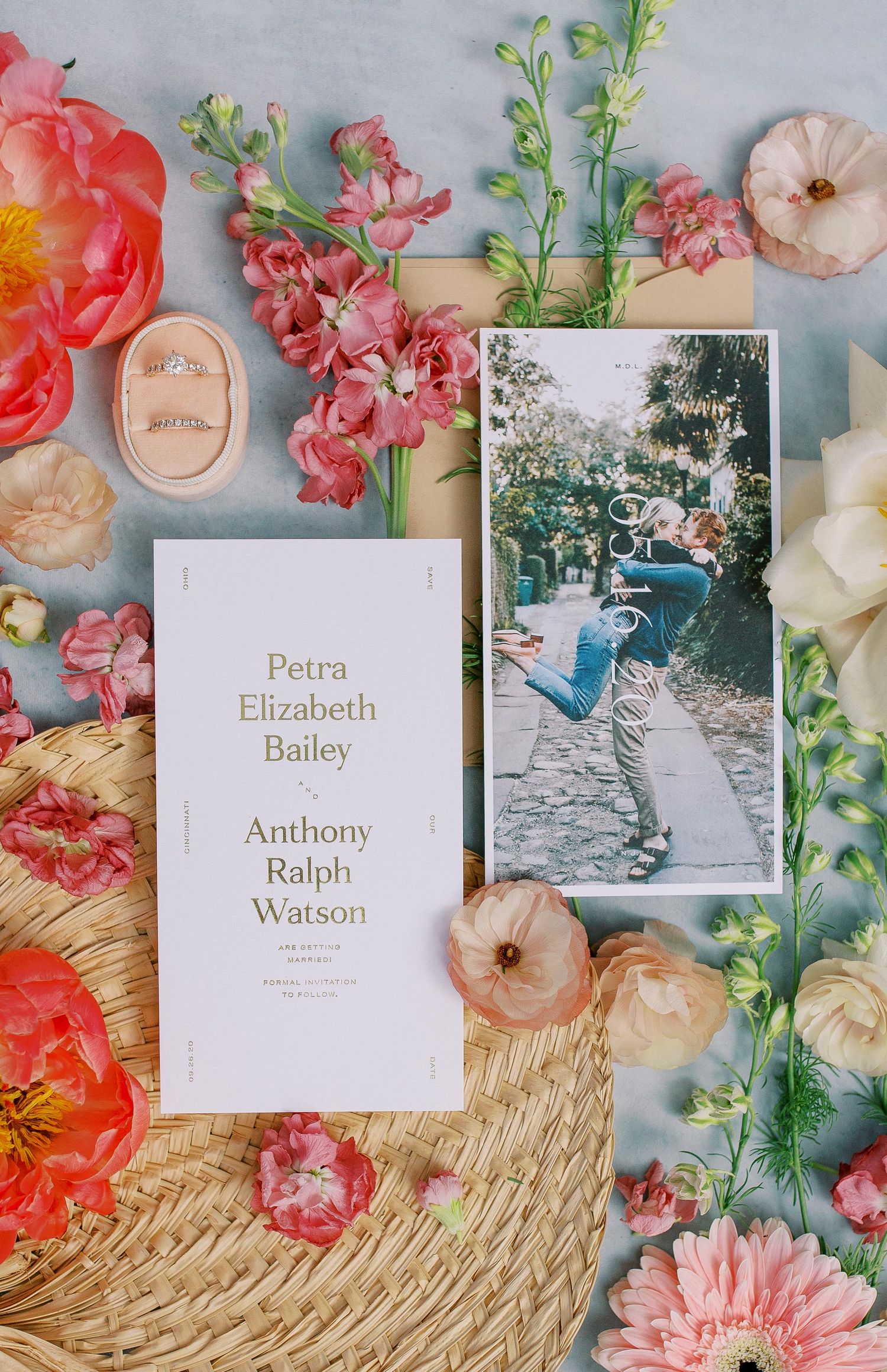 Wedding invitation suite with pink florals, a vintage photograph and delicate details arranged on a woven straw surface.