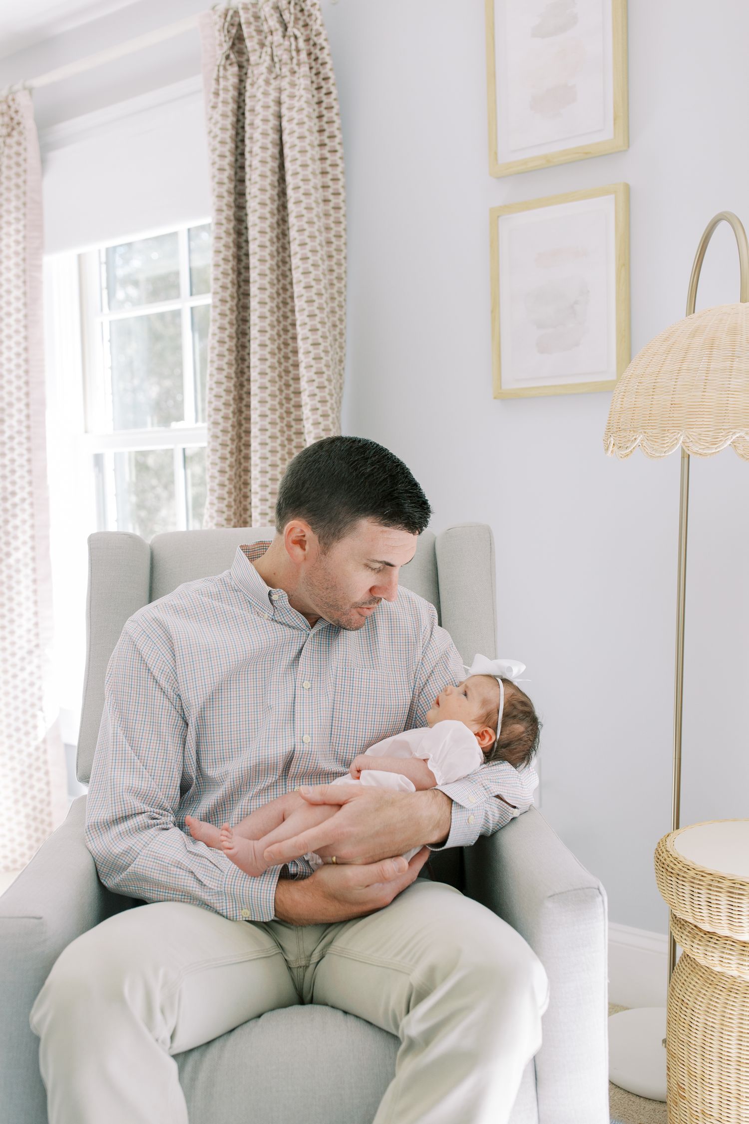 Adult in gray shirt cradling an infant in white in a cozy nursery setting.