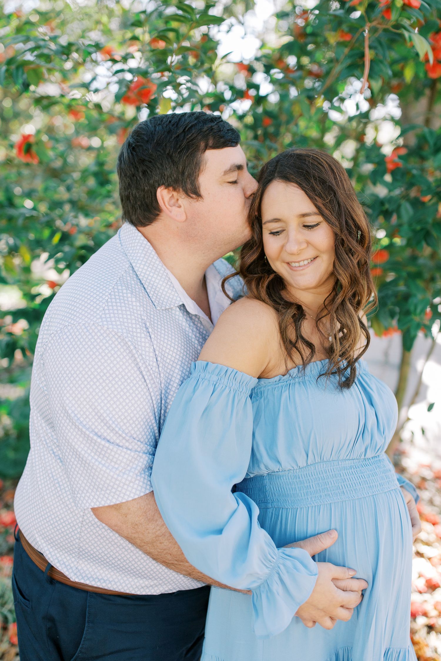A romantic moment captured under red berries as a couple embraces in coordinated blue and white outfits.