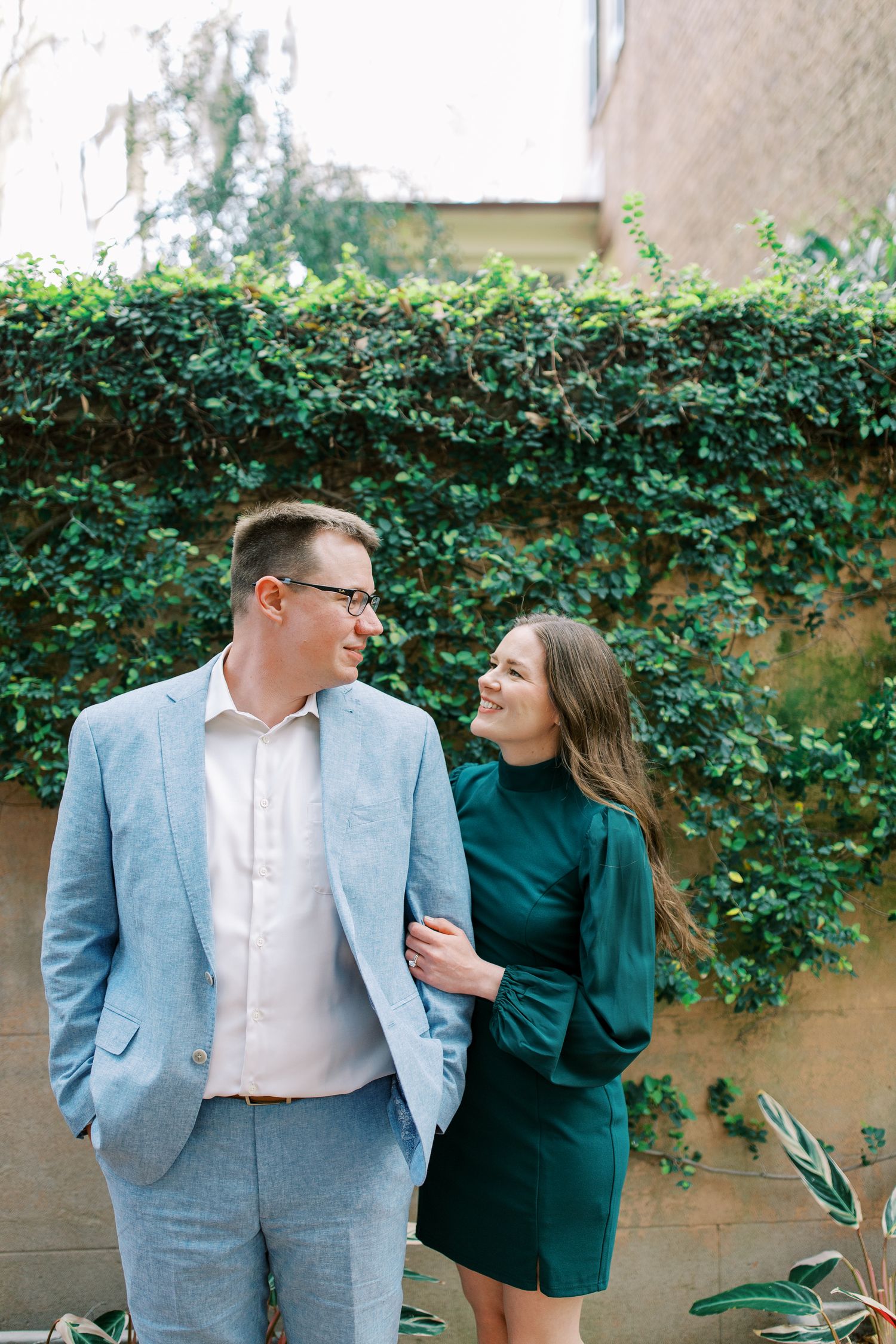 A couple shares a tender moment against a wall covered in lush green ivy.