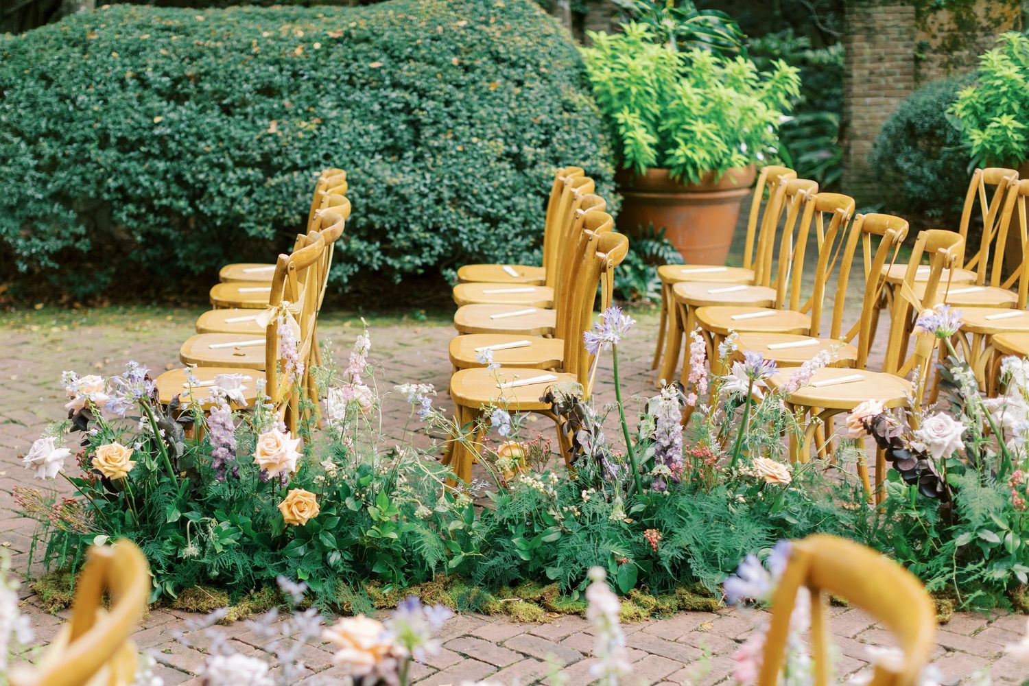 Elegant outdoor wedding ceremony setup with wooden chairs and floral arrangements in a garden setting.