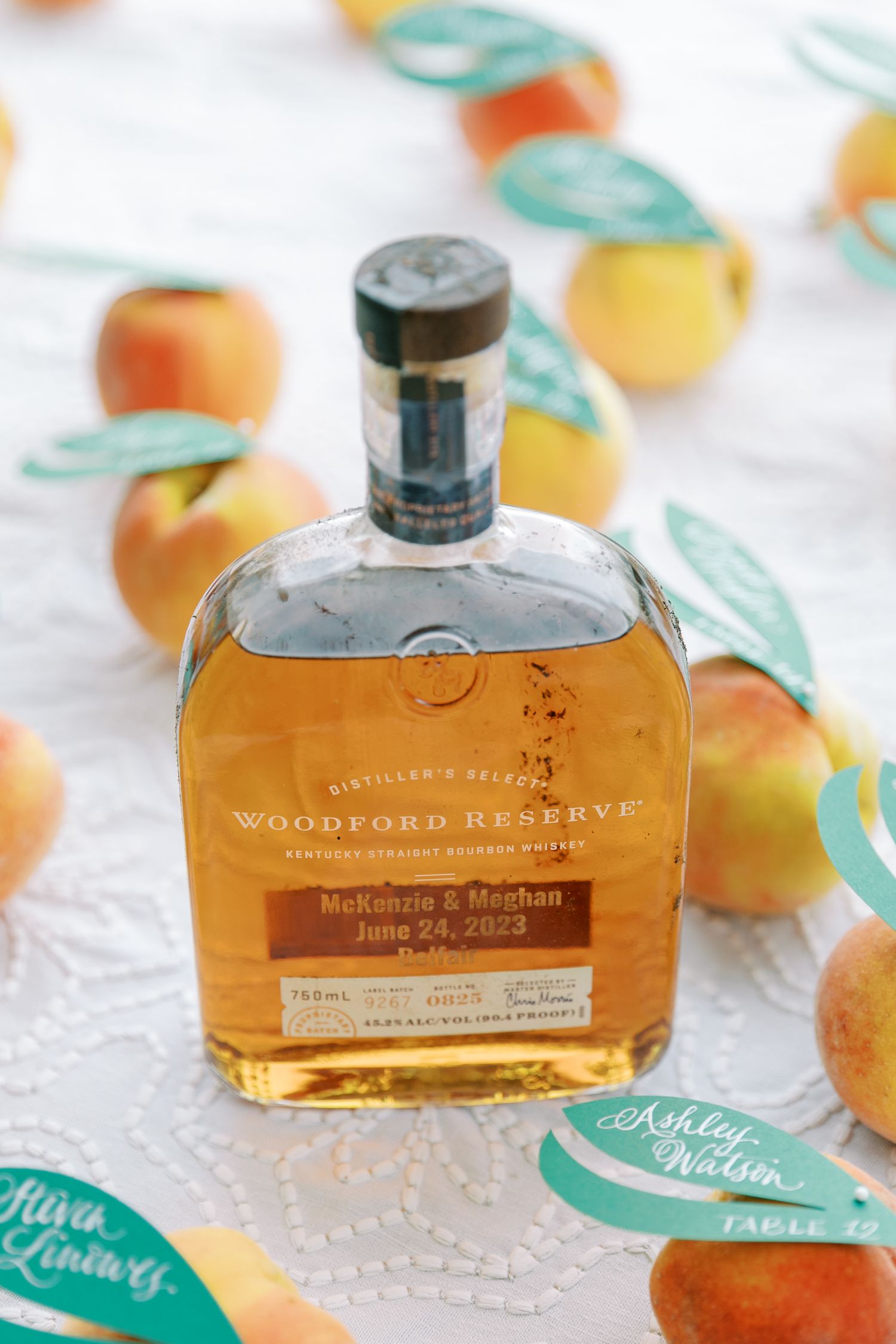 Personalized bottle of Woodford Reserve bourbon surrounded by peach decorations and teal name cards.