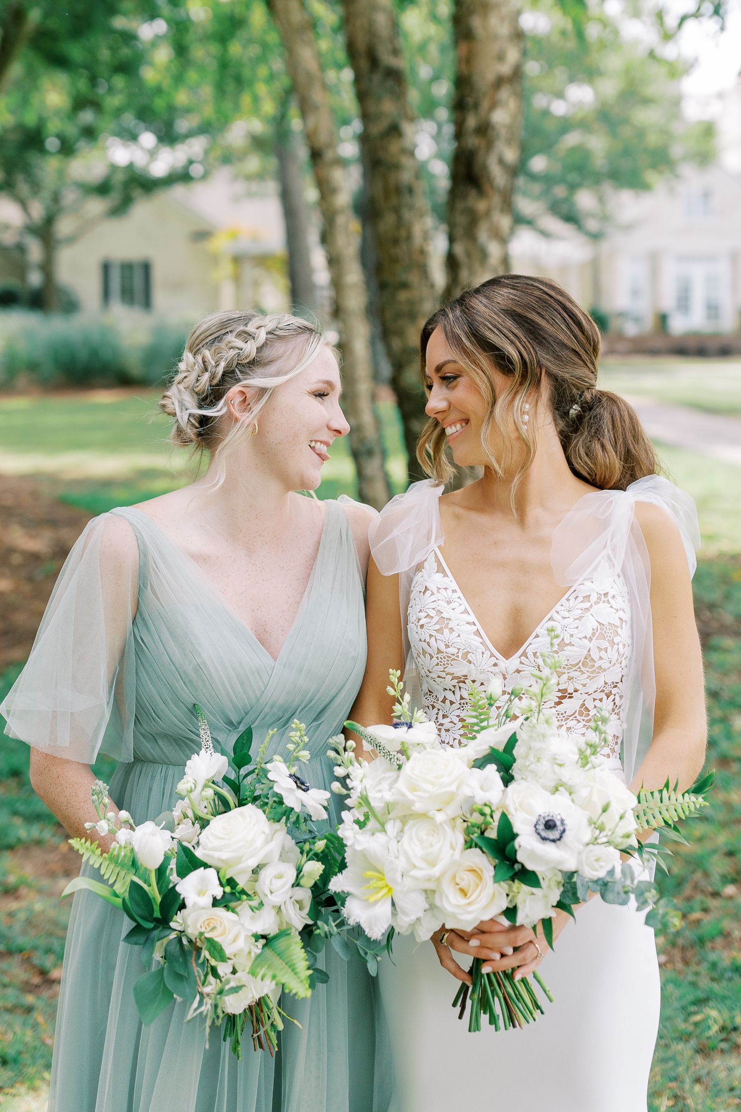 Wedding attendants in mint green and white gowns share a joyful moment while holding elegant floral bouquets.