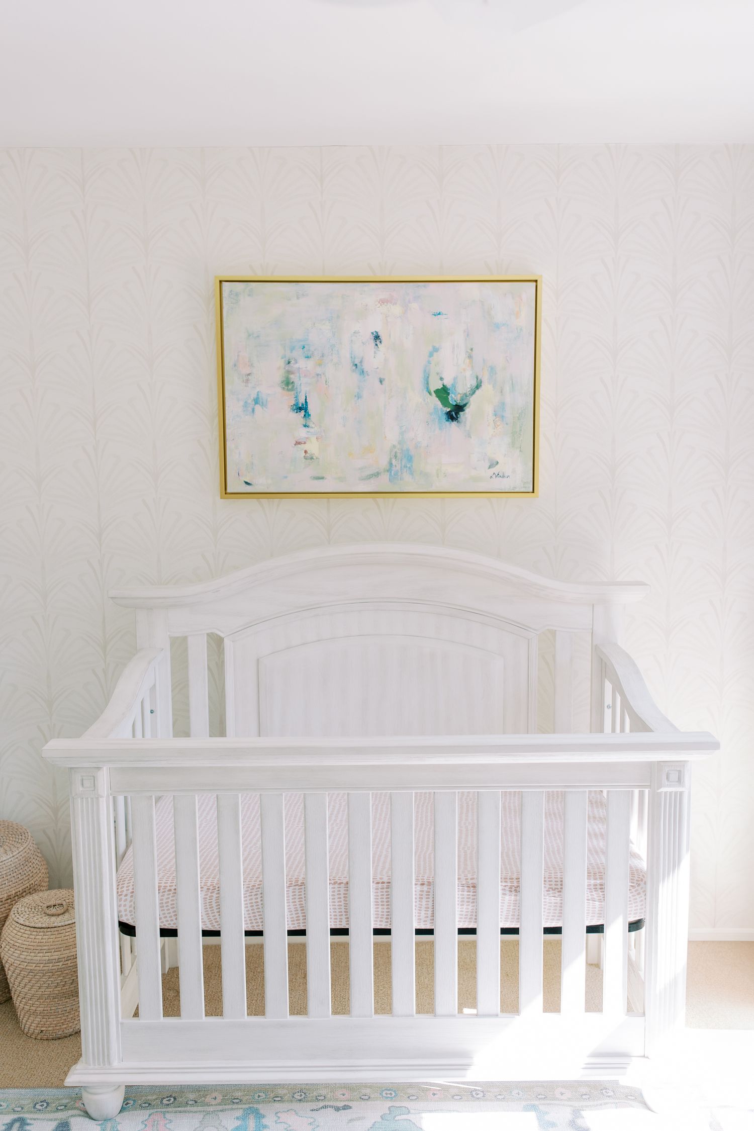 White wooden baby crib with an abstract watercolor artwork in soft blue and green tones hanging above it.