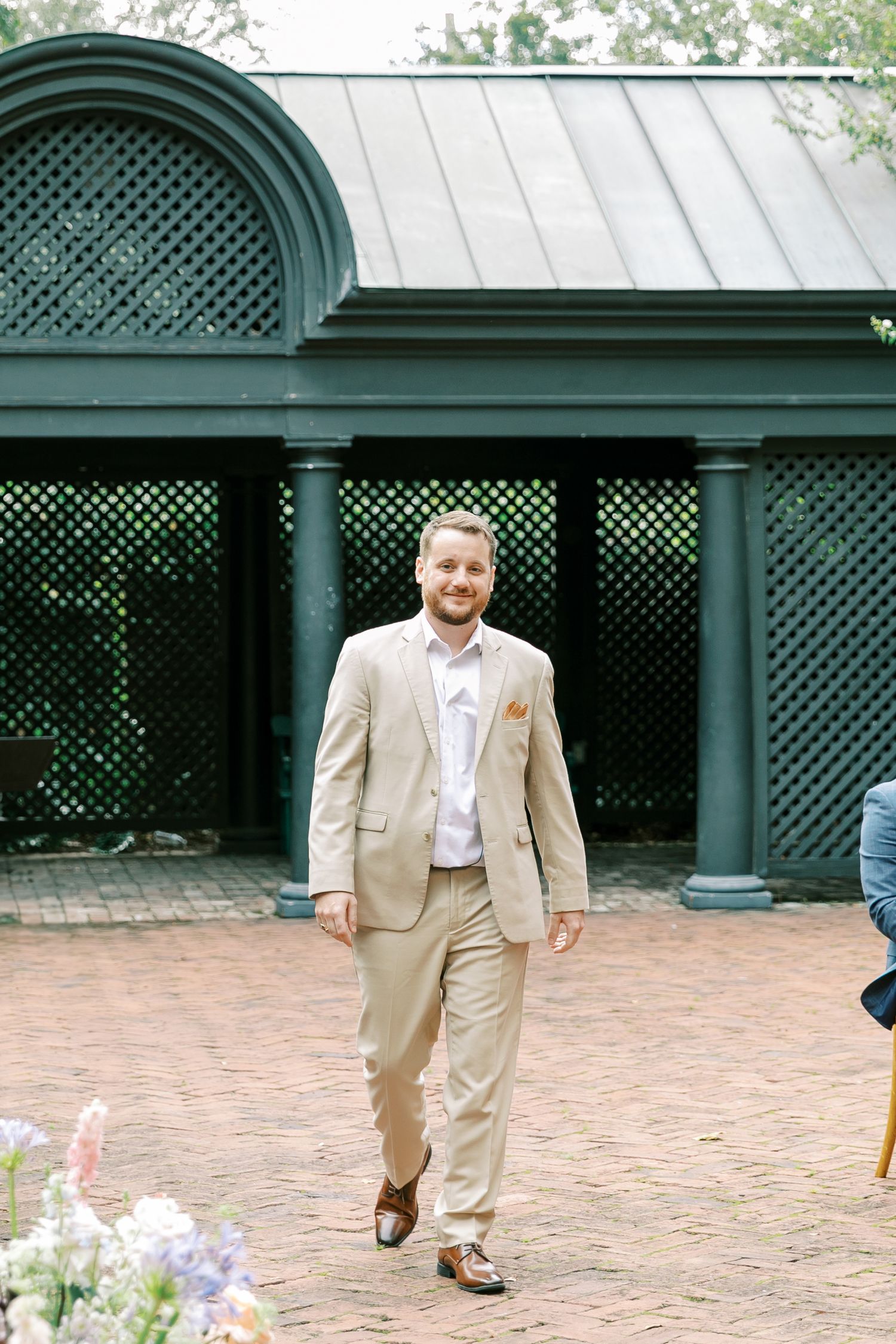 Men in tan suits walk across a brick courtyard with lattice architecture.
