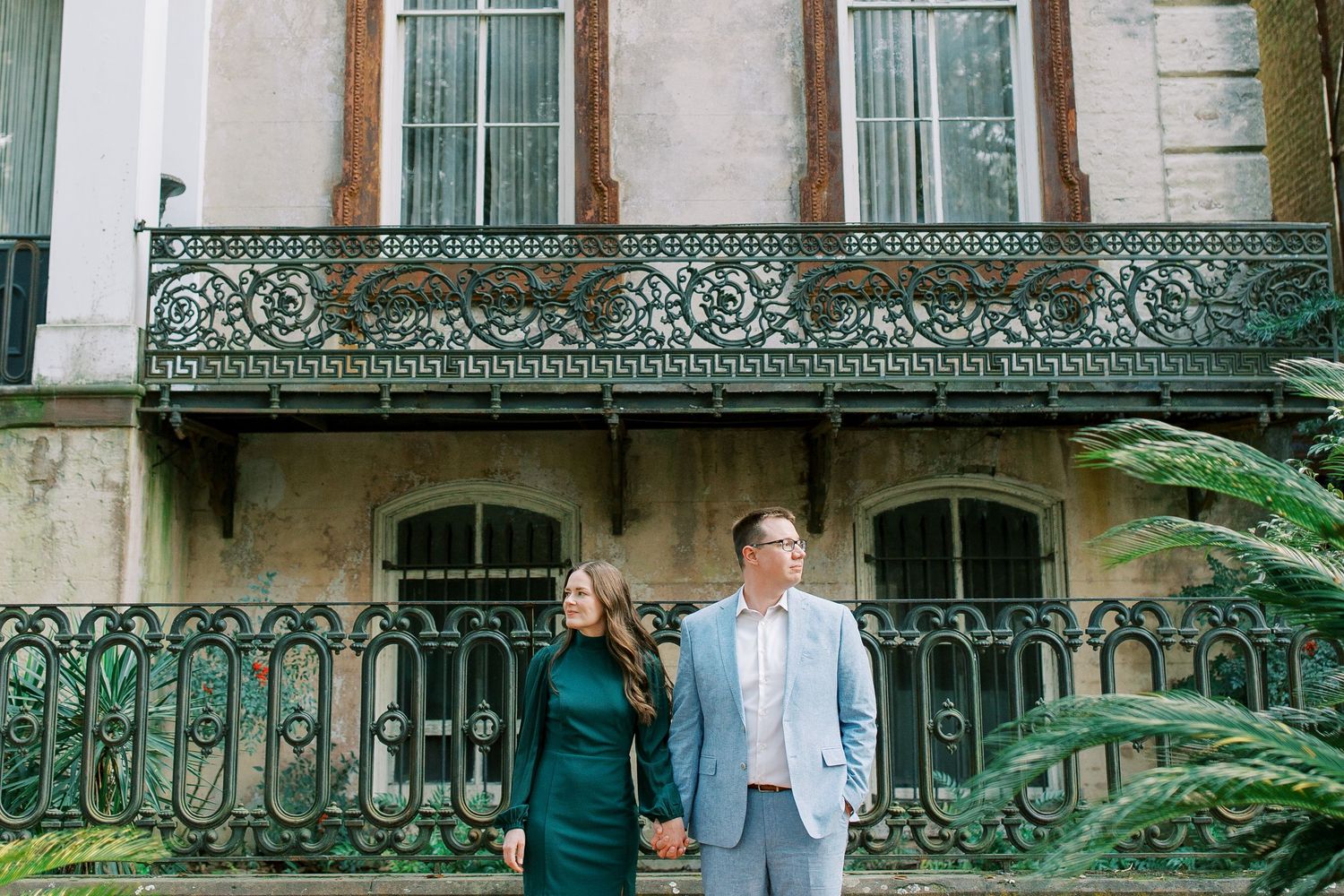 Two people stand on the steps of a historic house with ornate green ironwork balcony in Savannah, Georgia.
