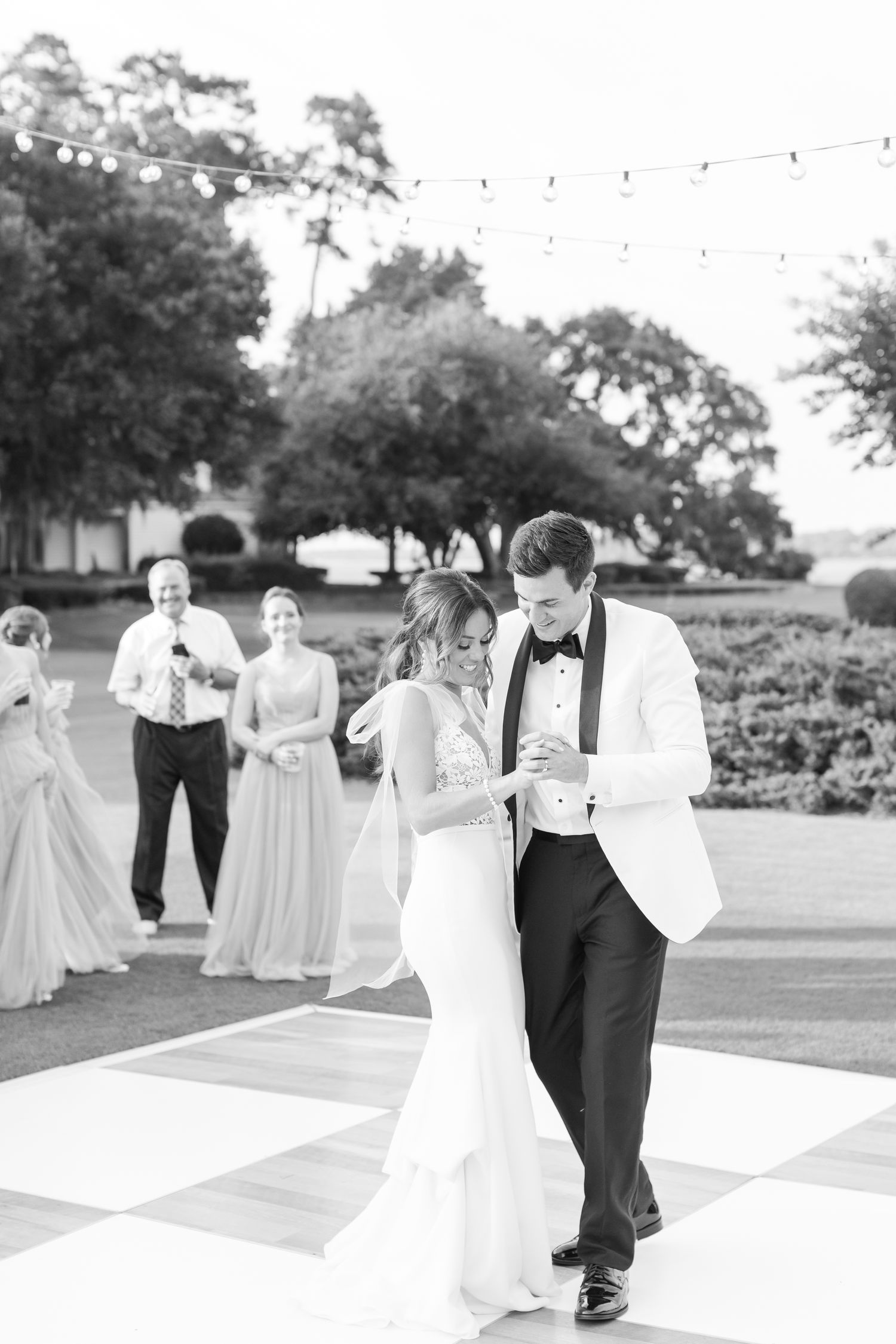 A couple shares their first dance on a black and white checkered dance floor at an elegant outdoor wedding reception.