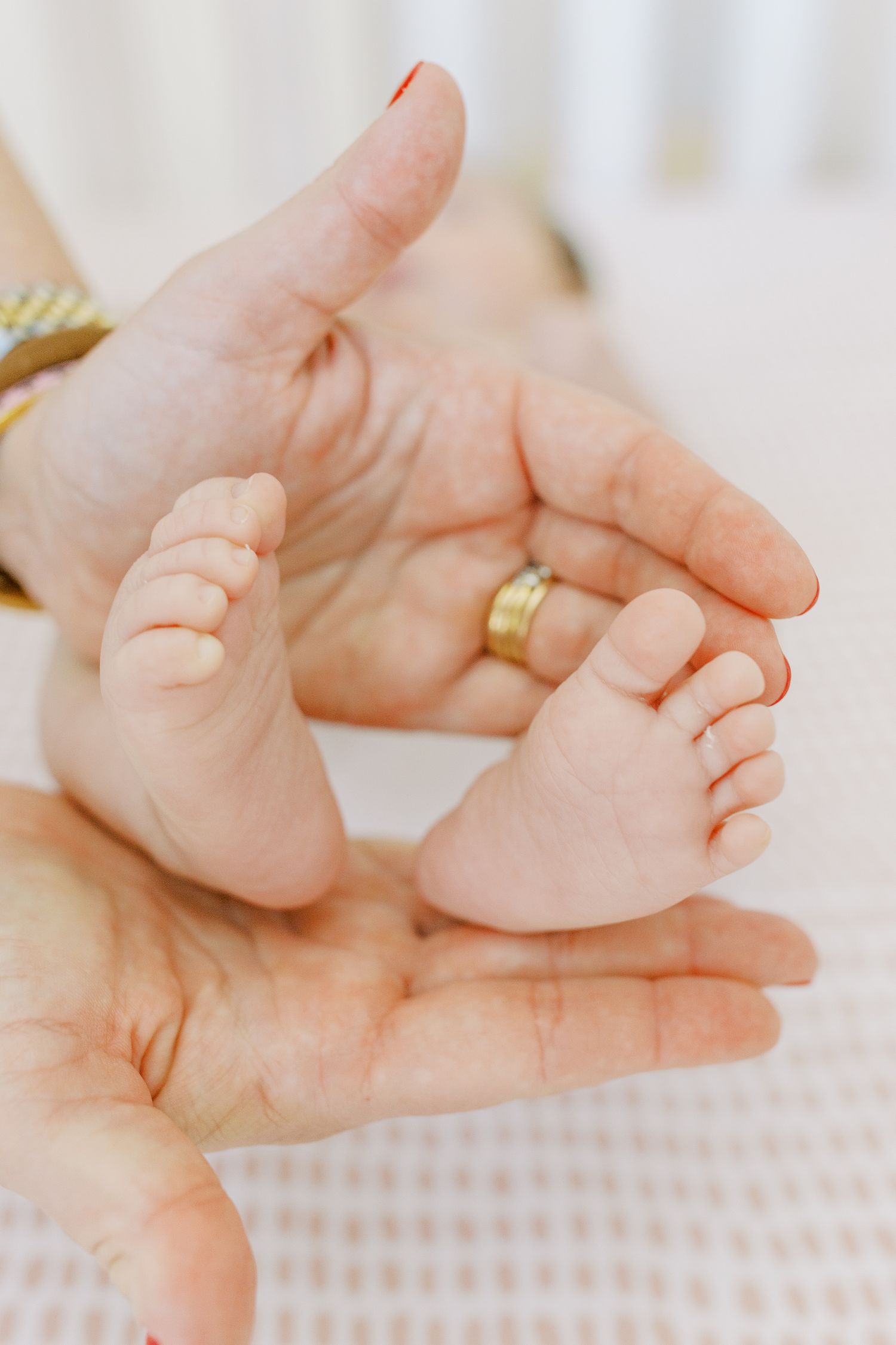Tiny baby feet resting in adult hand wearing gold ring against white background.
