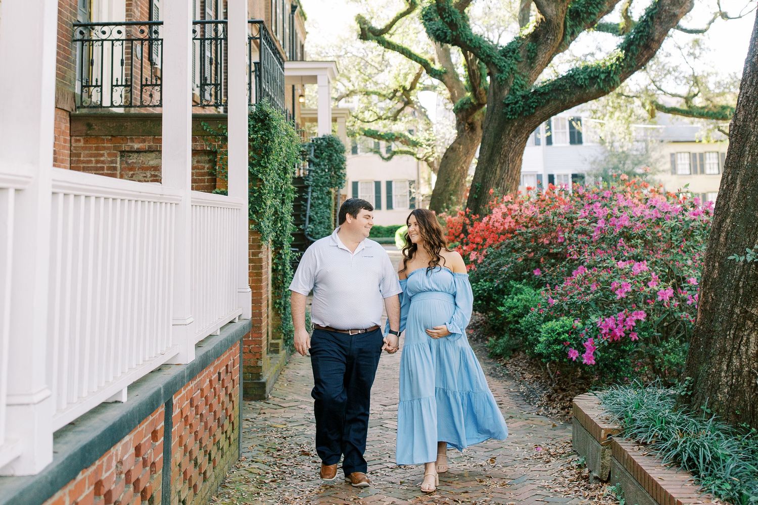 A couple strolls down a charming Charleston sidewalk lined with blooming azaleas and live oak trees.