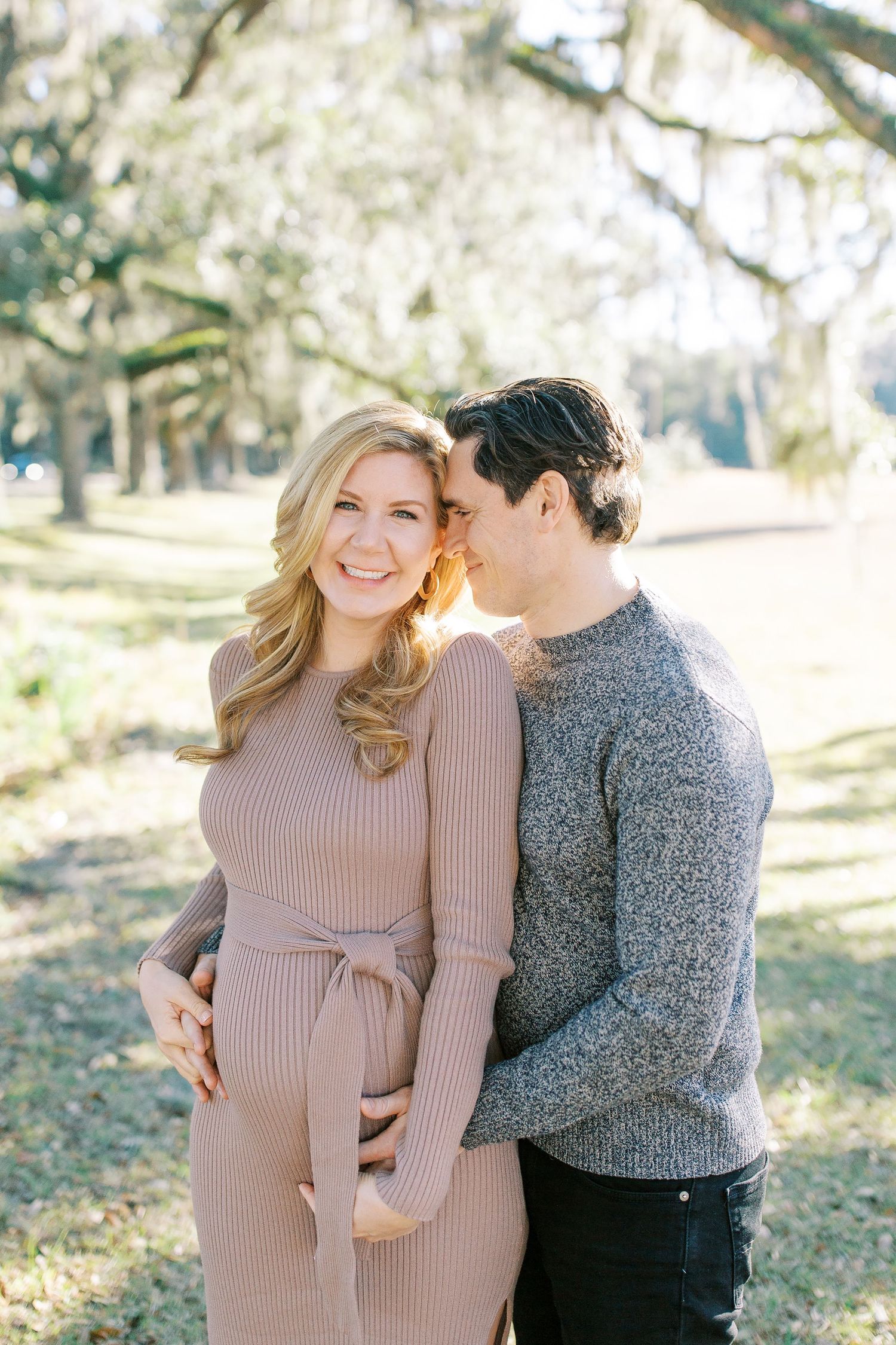 Couple embraces outdoors in romantic photoshoot with Spanish moss and trees in background.