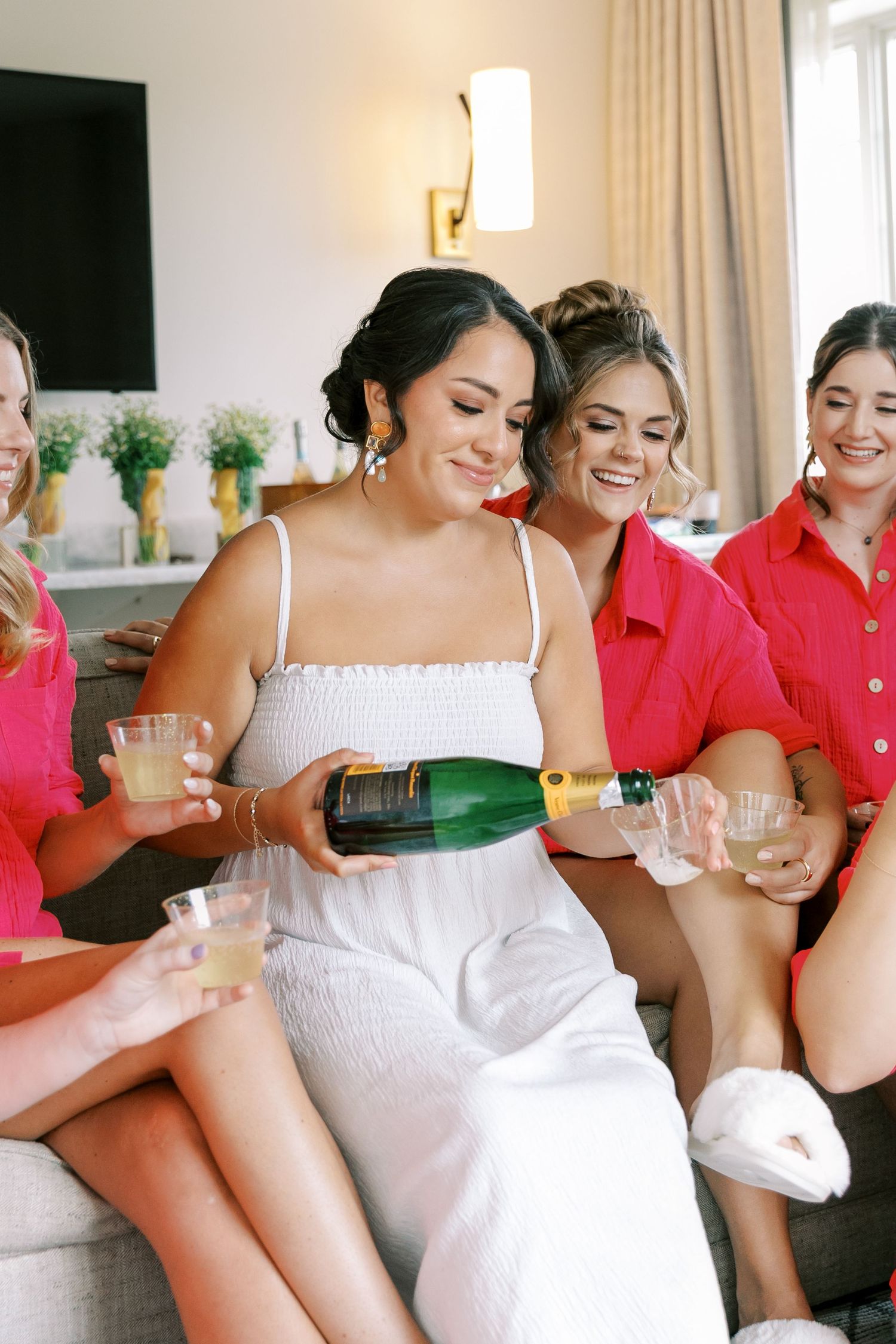 Group celebrates with champagne while wearing white and coral outfits in a bright indoor setting.
