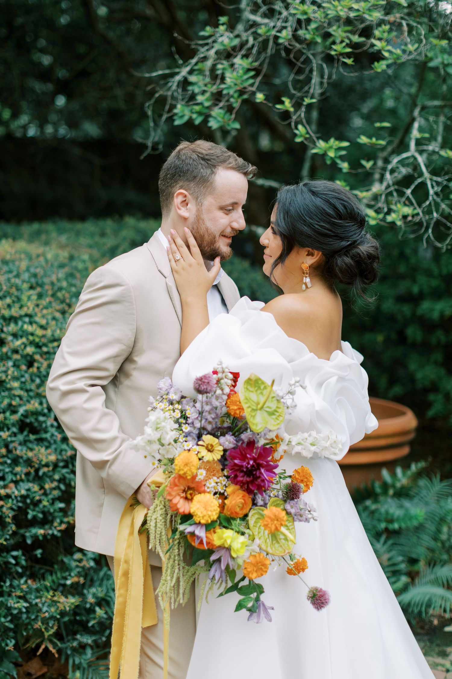 A romantic wedding portrait featuring a colorful wildflower bouquet with orange, purple and yellow blooms in a garden setting.