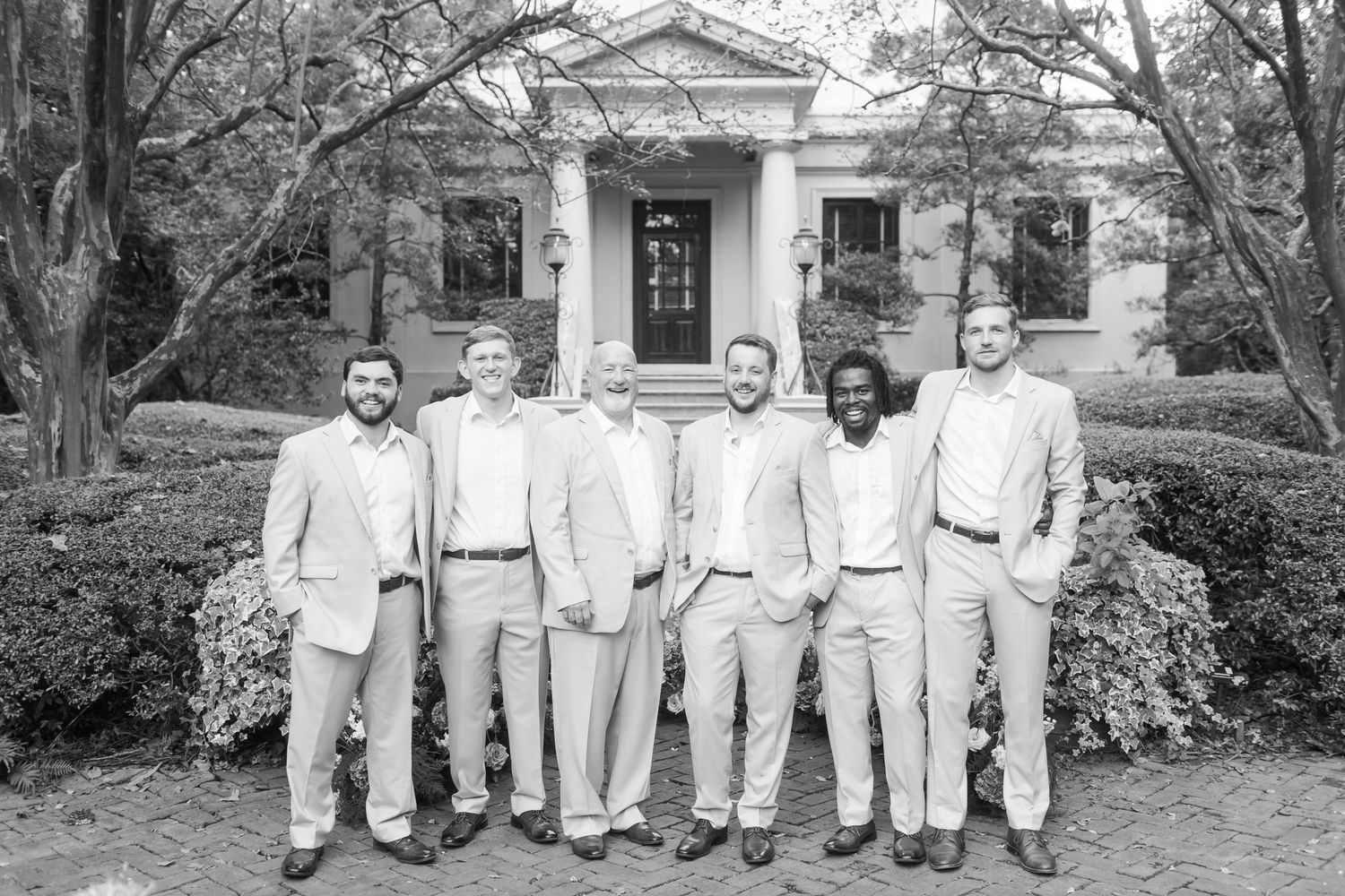 Wedding party members in light colored attire pose in front of a historic white building.