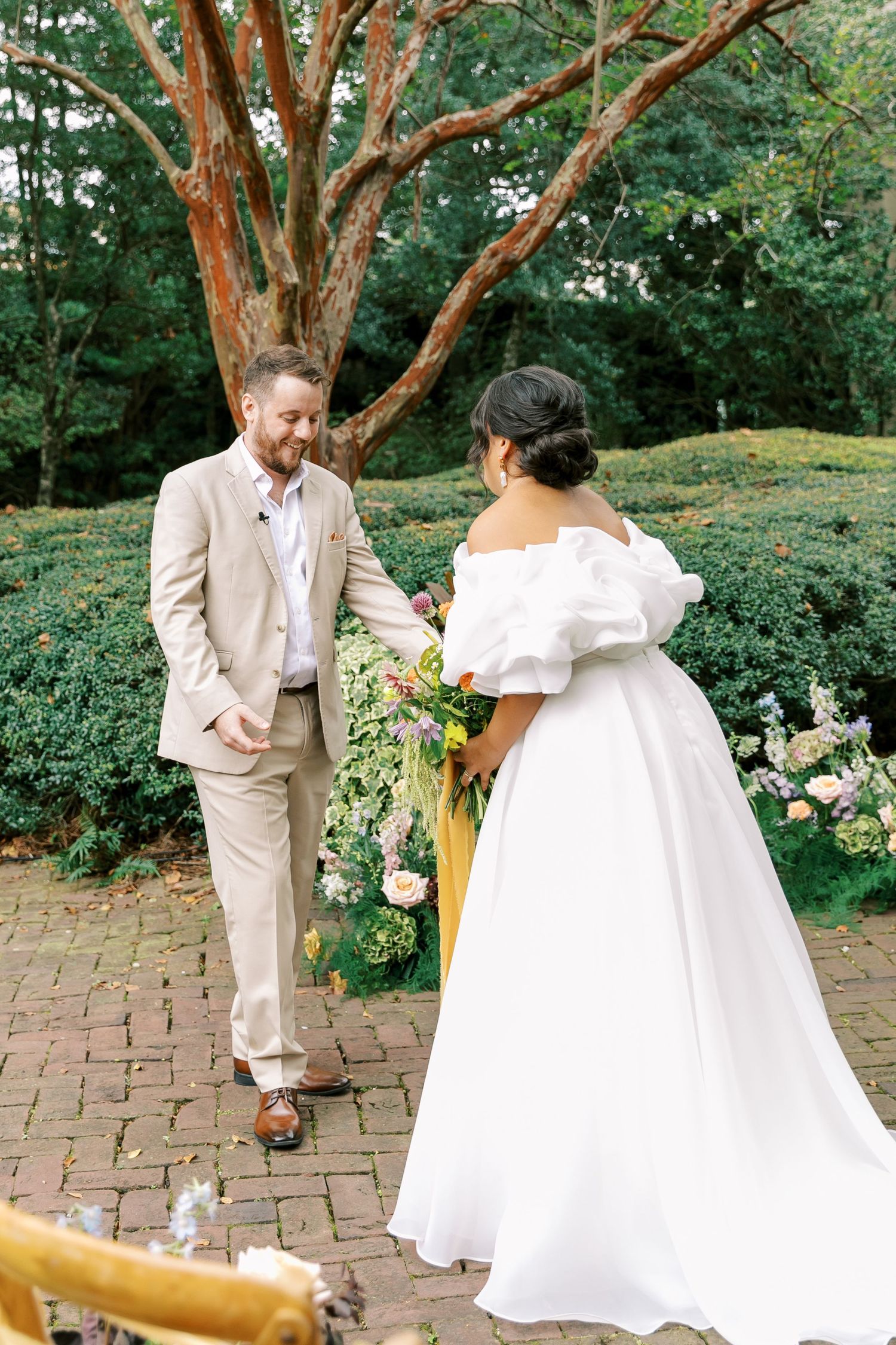 A romantic first look moment between newlyweds in a garden setting with brick pathways and lush greenery.