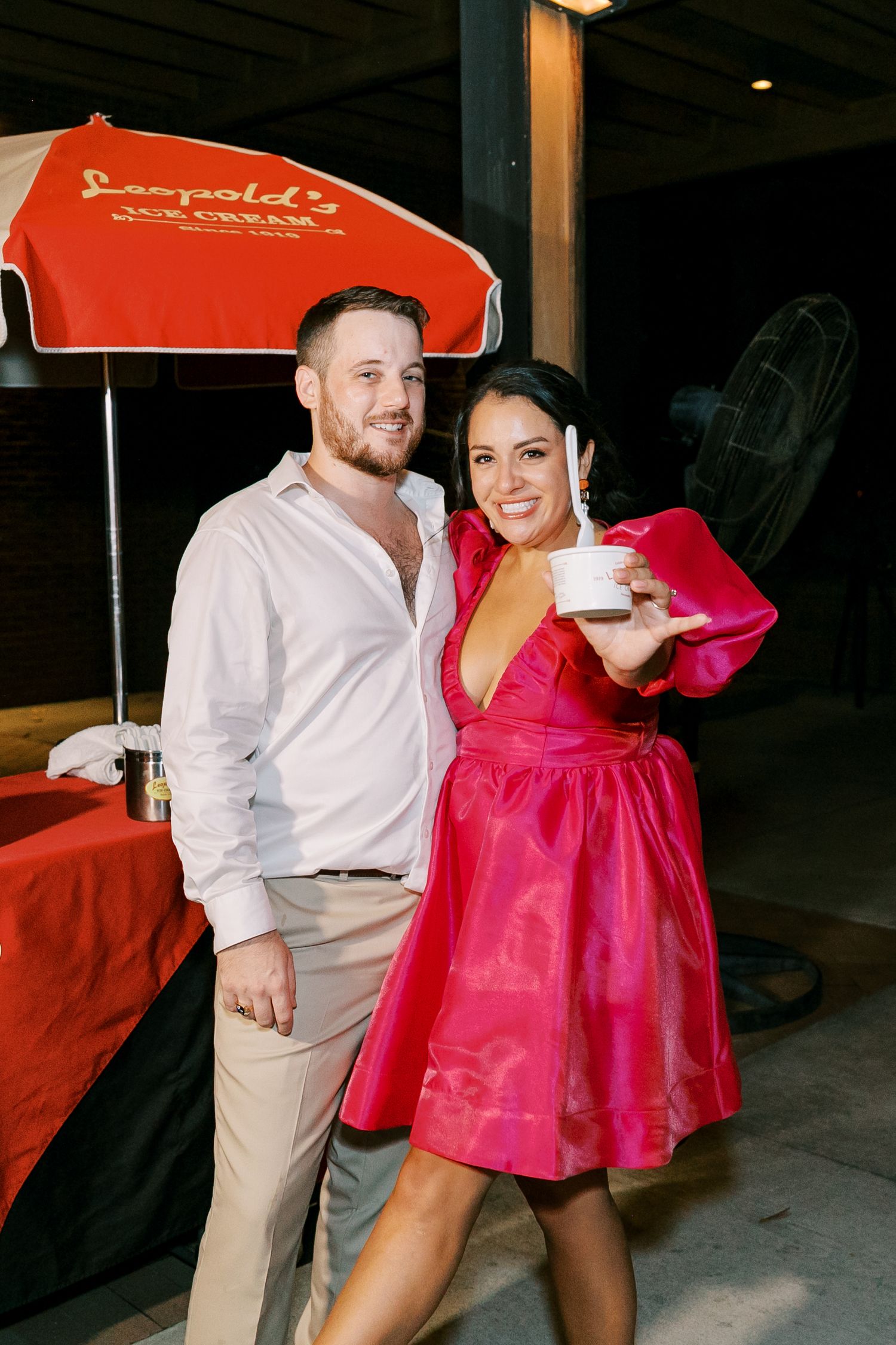 A couple poses beneath a red umbrella at their wedding reception celebration.