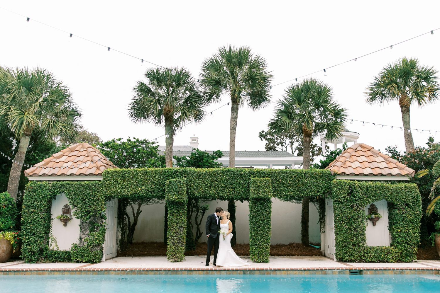 Elegant outdoor venue with ivy-covered pavilion and palm trees surrounding a swimming pool during a wedding portraits in St. Simons, GA.
