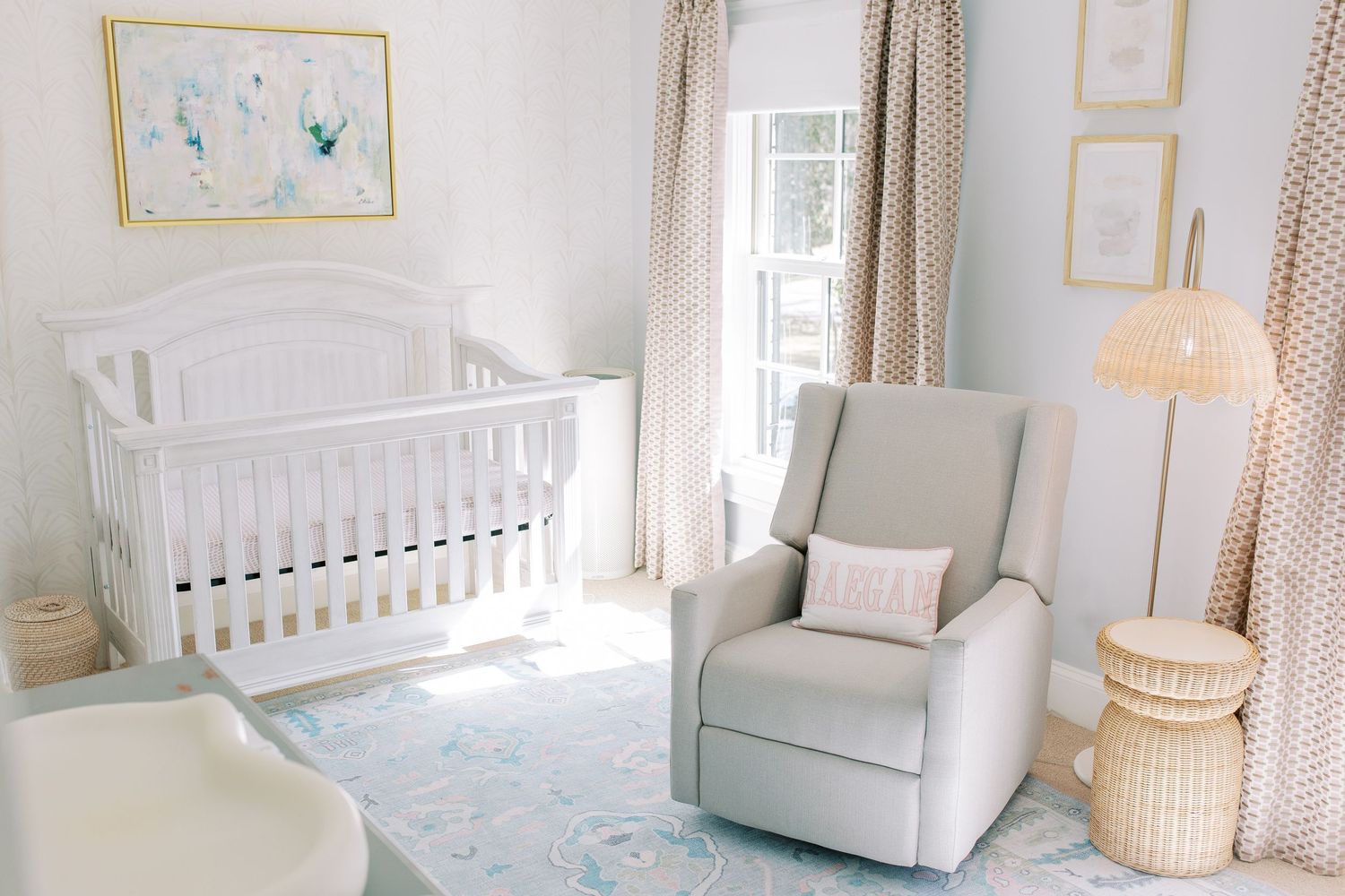 A bright neutral nursery with white crib, gray recliner, patterned rug, and soft curtains in a minimalist style.