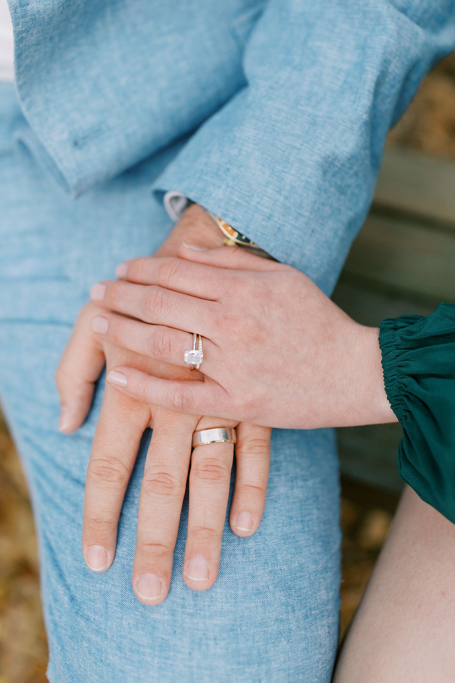 Close-up of hands wearing engagement rings with one hand resting on light blue fabric.
