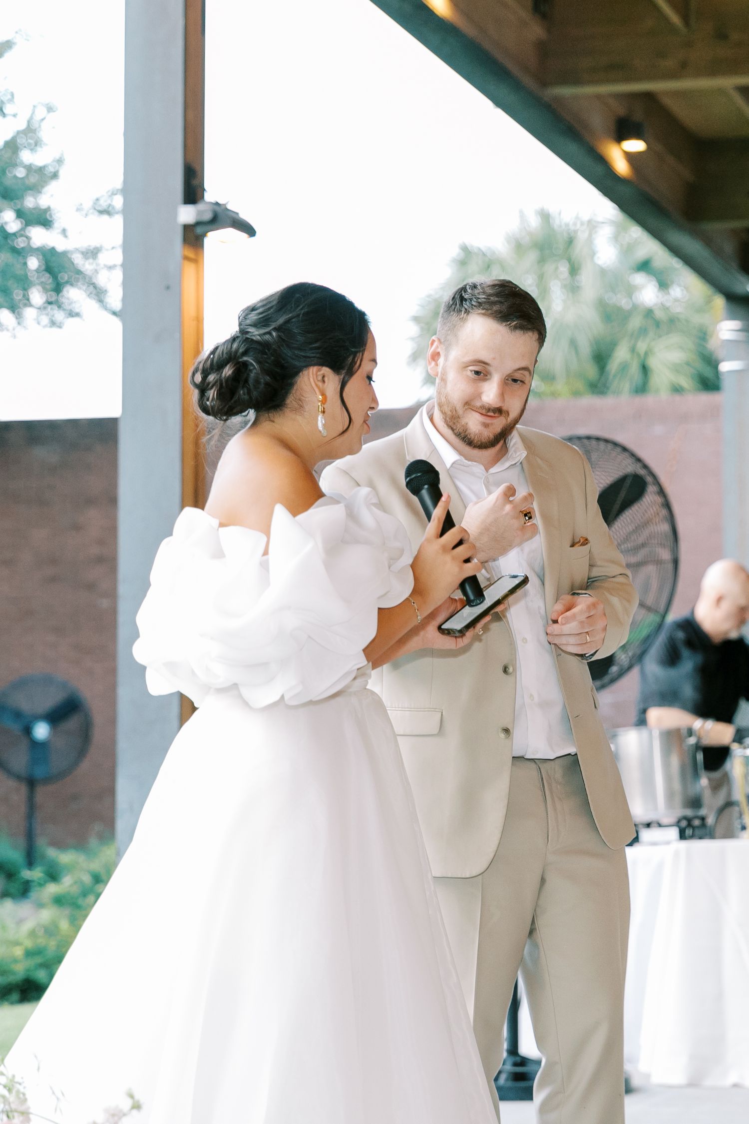 Wedding couple shares an emotional moment during reception speeches under covered outdoor venue.