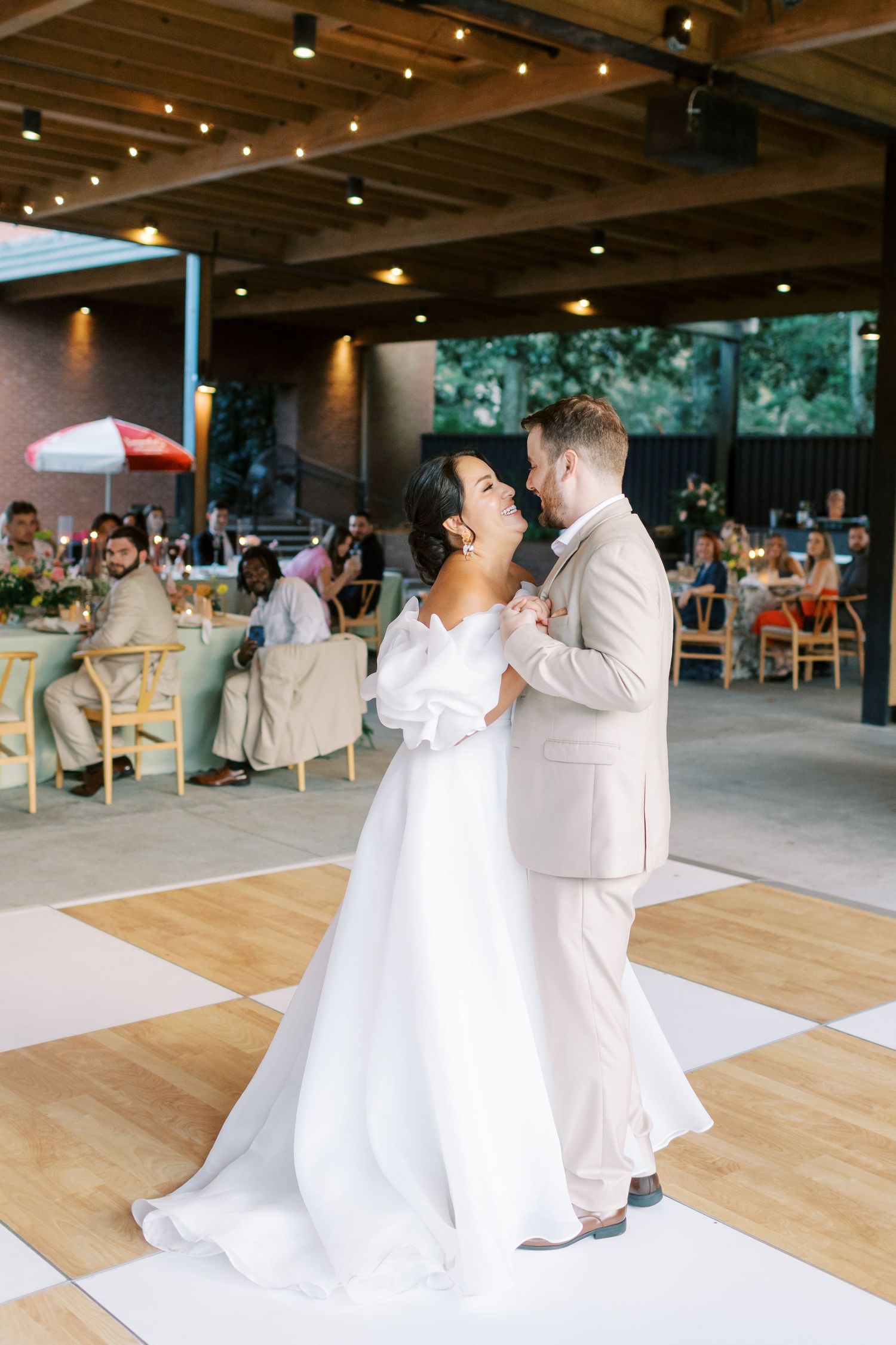 A couple shares their first dance on a wooden floor during their wedding reception.