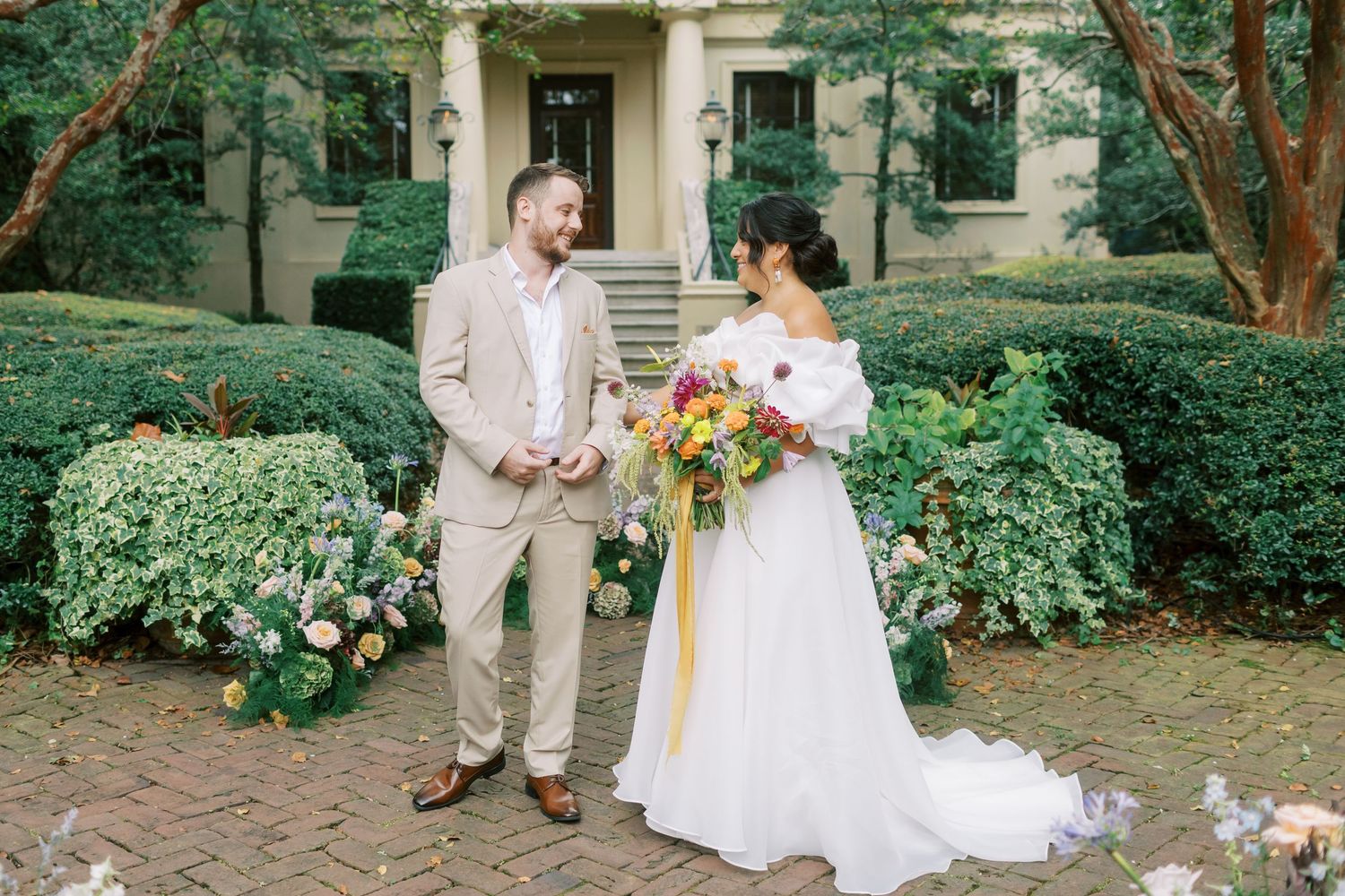Newlyweds share a moment on brick path surrounded by lush garden landscaping.