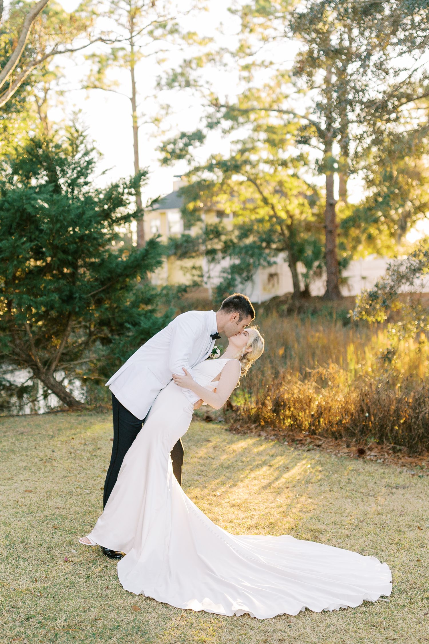 A romantic golden hour outdoor wedding photo featuring a couple embracing in formal attire with a flowing white gown.