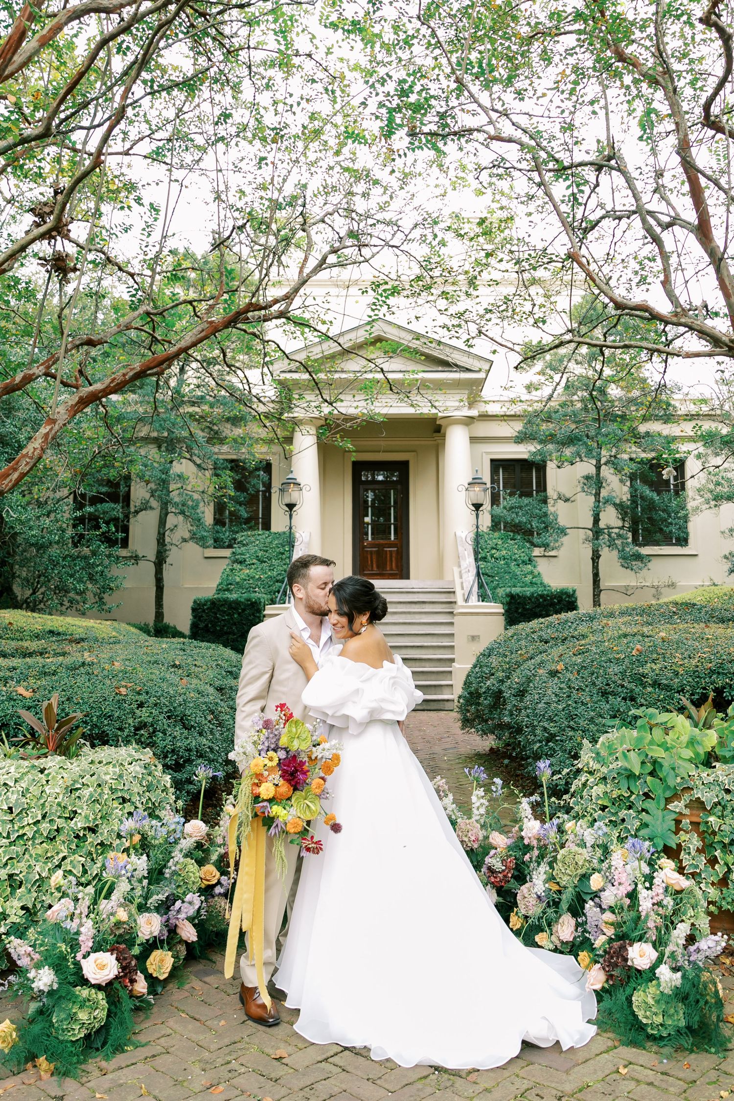 Newlyweds pose for romantic portraits in a lush garden setting with blooming flowers.