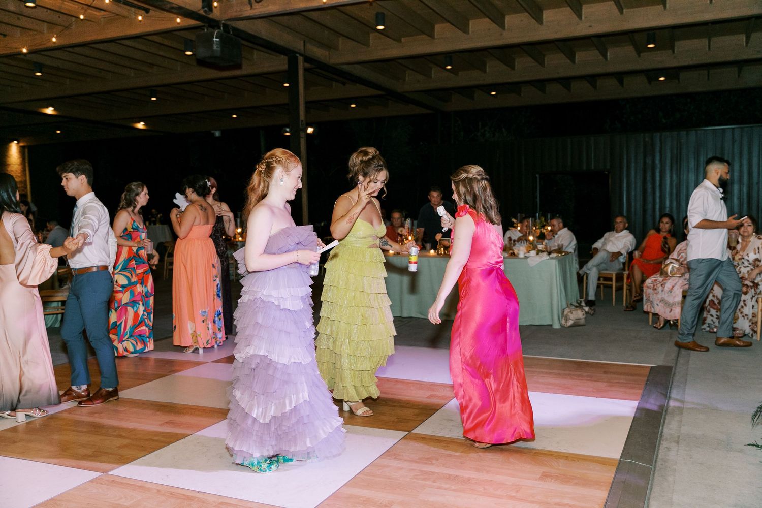 Wedding guests dancing in colorful pastel dresses on a checkered dance floor.