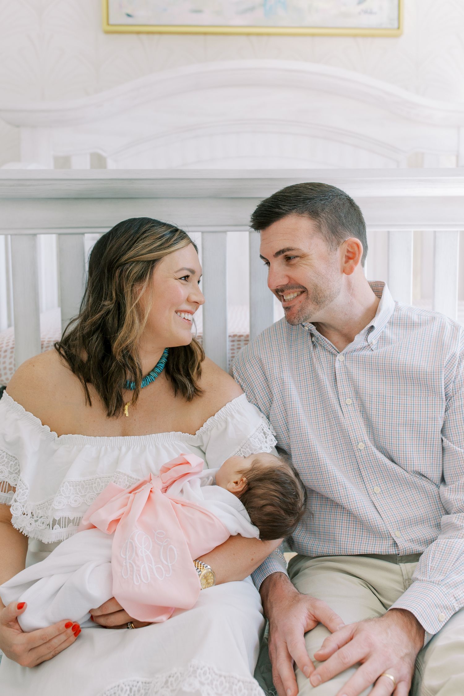 Family shares intimate moment while sitting together on white crib in nursery setting.