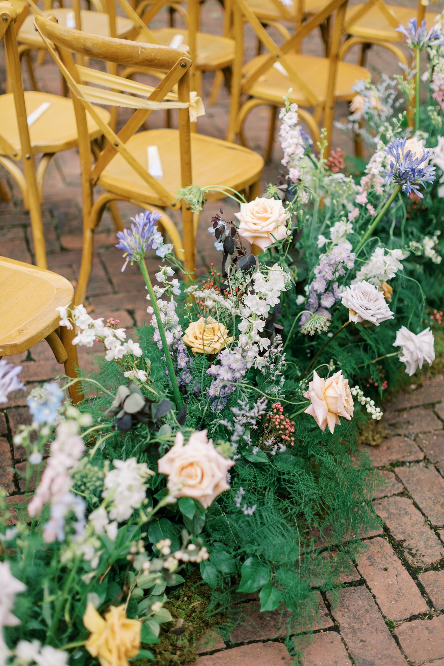 Delicate floral arrangements with roses and wildflowers line the aisle next to wooden chairs.
