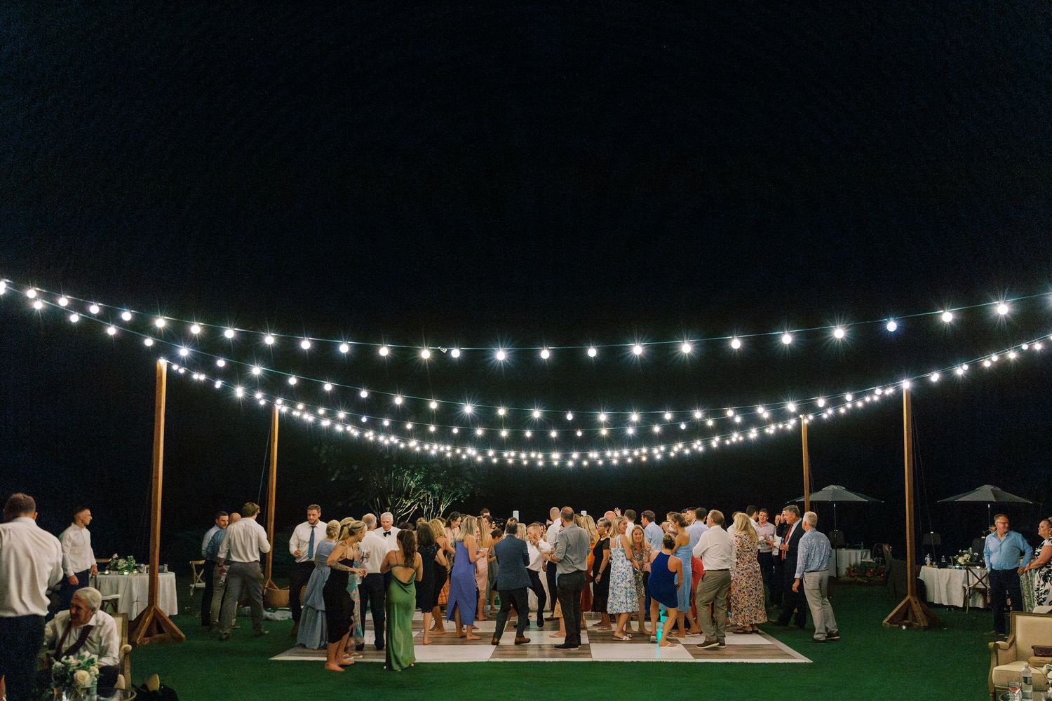Outdoor evening reception with string lights illuminating dance floor.