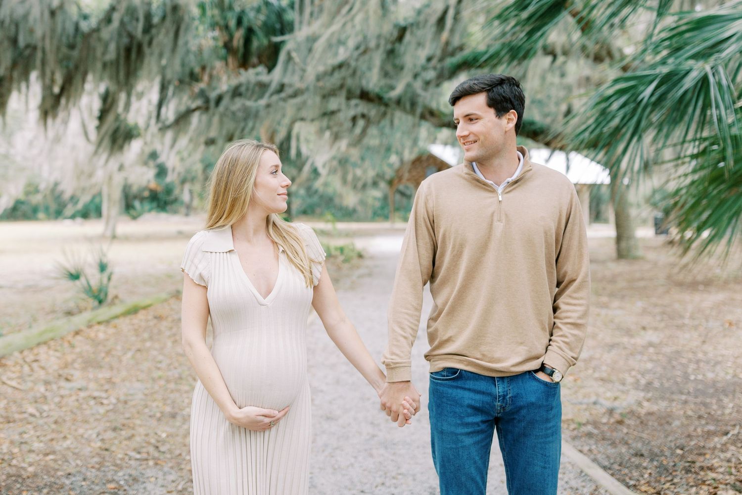 A couple walks hand in hand along a woodland path surrounded by palm trees and greenery.