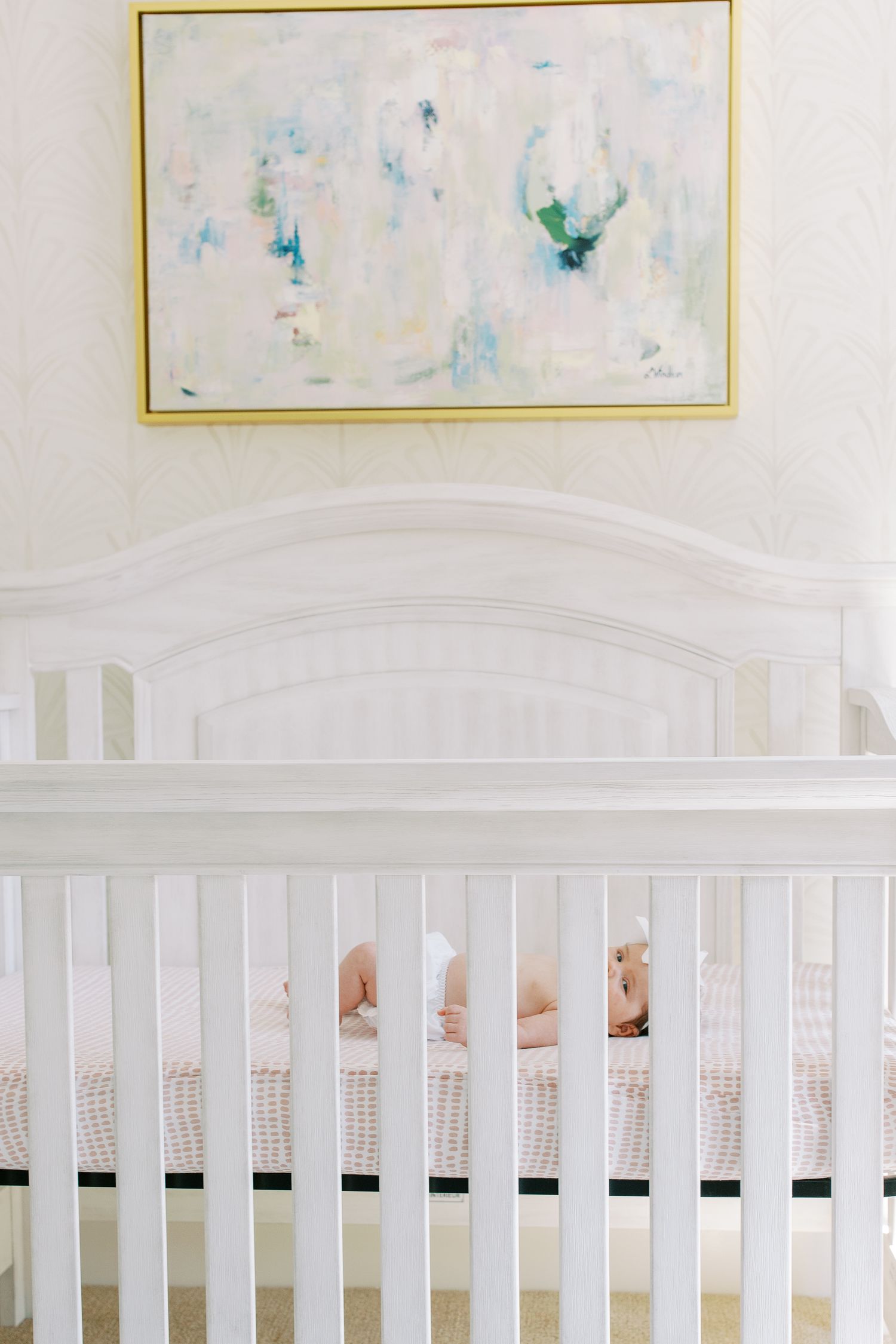 White crib with abstract blue and green artwork hanging above in nursery.