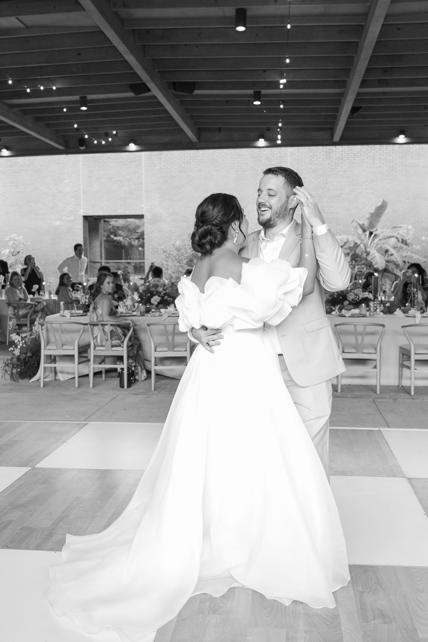 A romantic first dance moment on a checkered dance floor under string lights at a wedding reception.