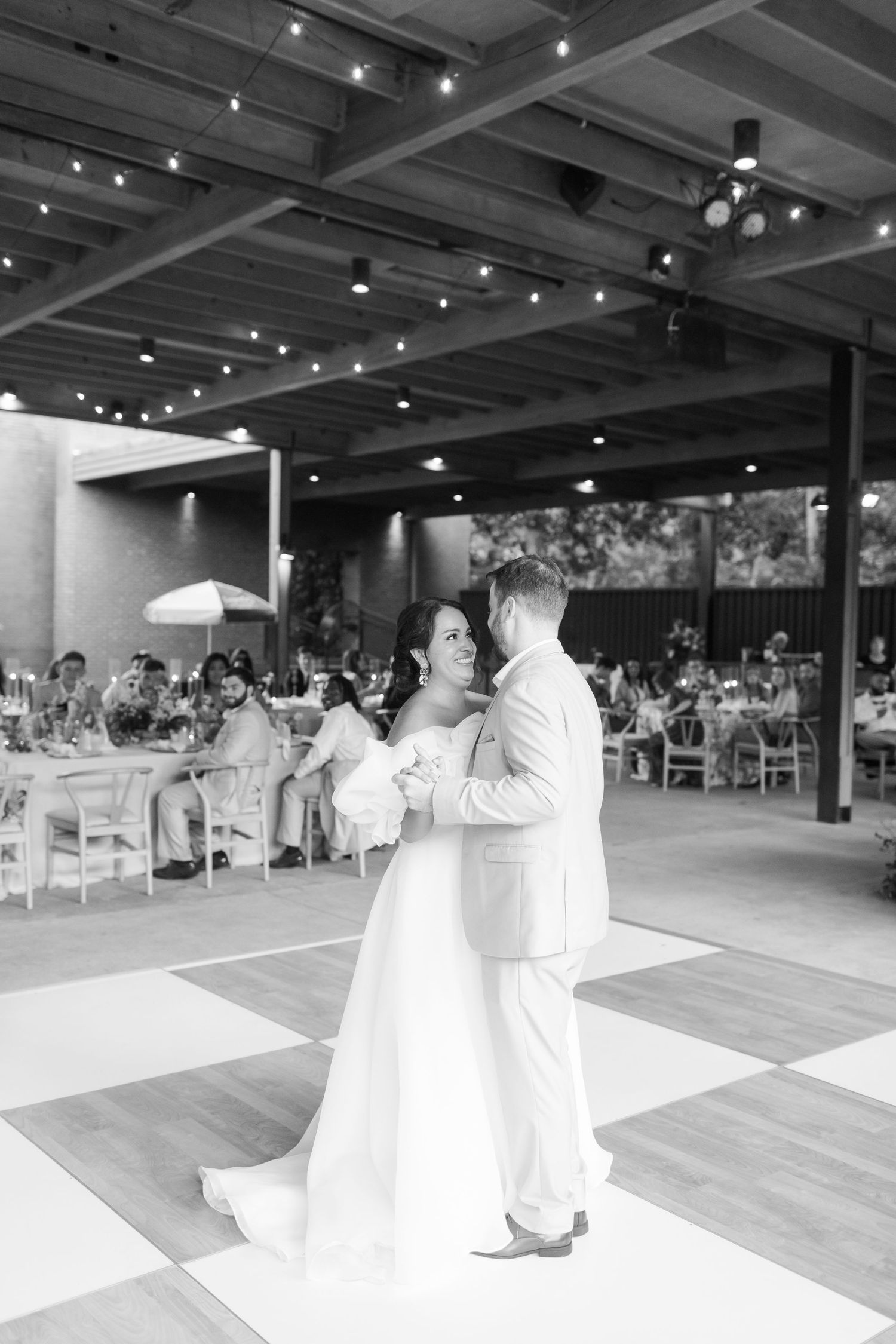 A romantic first dance captured in black and white under twinkling lights at a wedding reception.